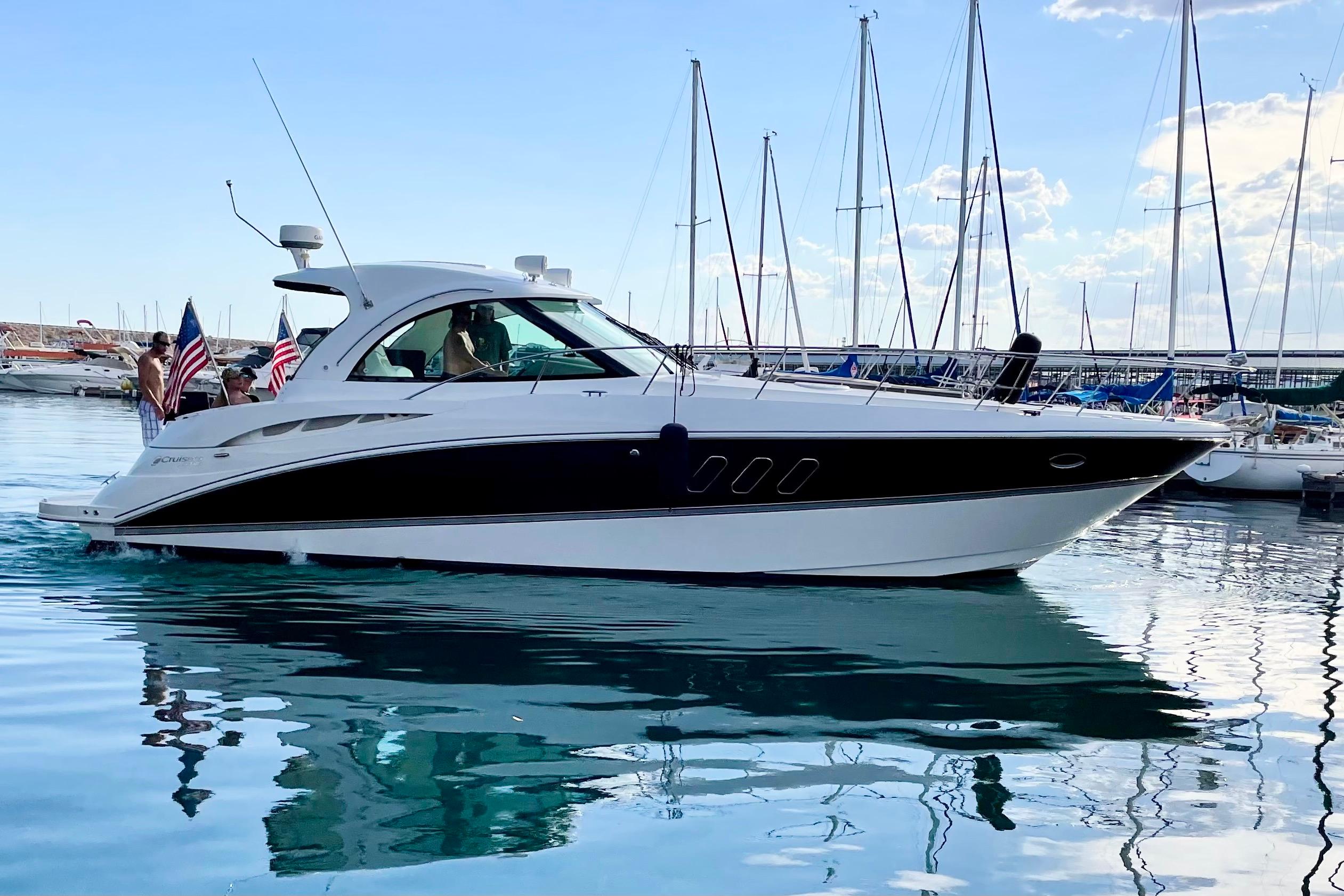 2011 Cruisers Yachts 390 Sports Coupe on calm water, with flags and marina backdrop.
