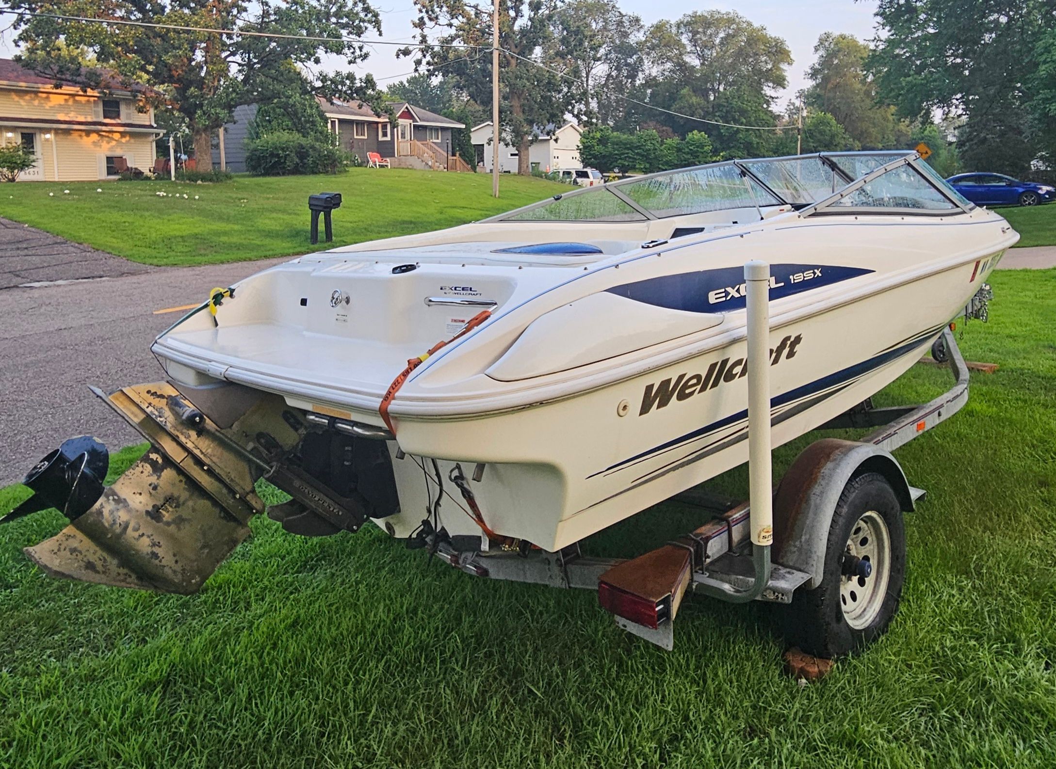 A 1996 Wellcraft Excel boat on a trailer, parked on a grassy lawn.