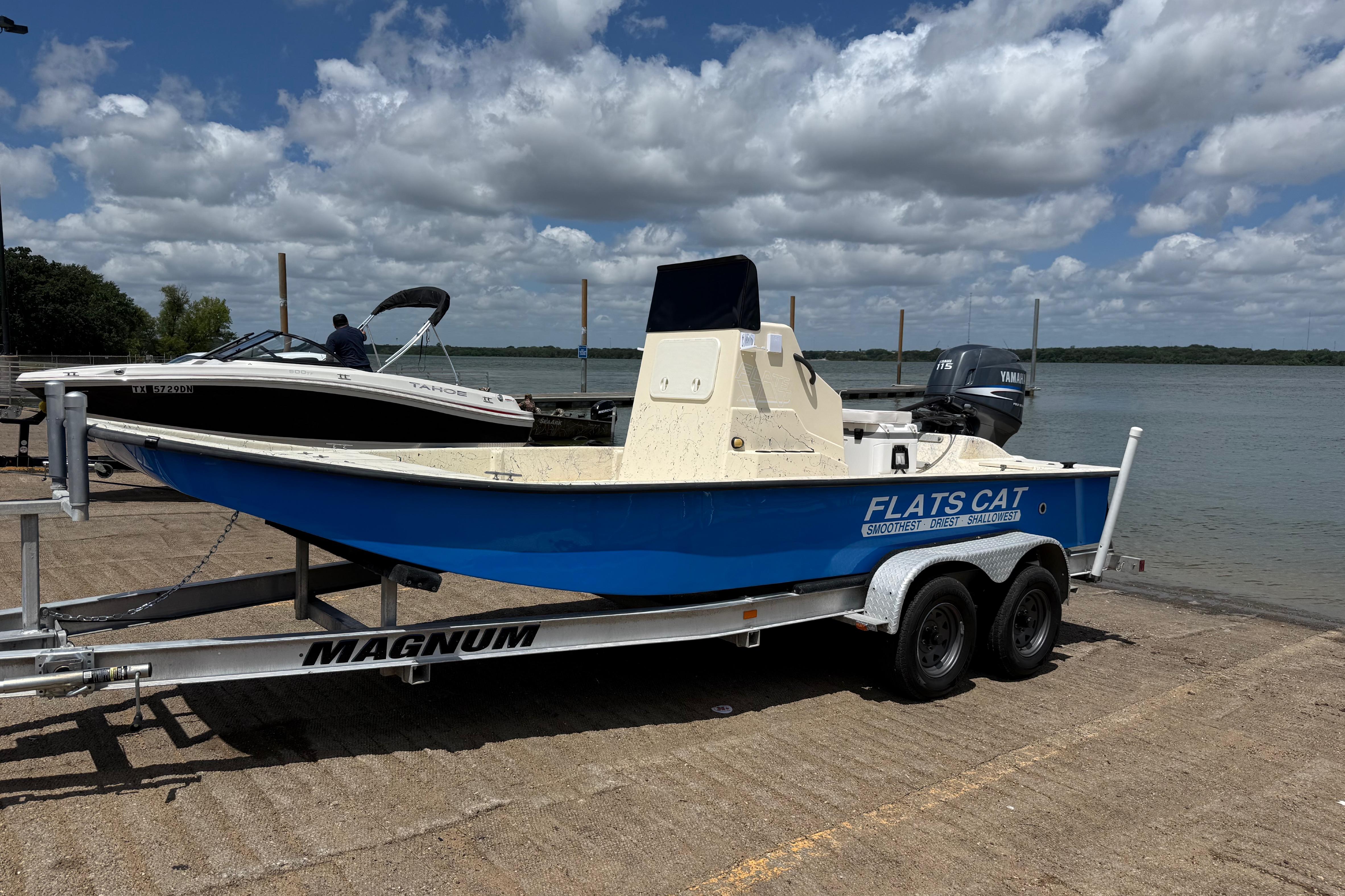 2007 Flats Cat 19 boat on trailer by lake under cloudy sky.