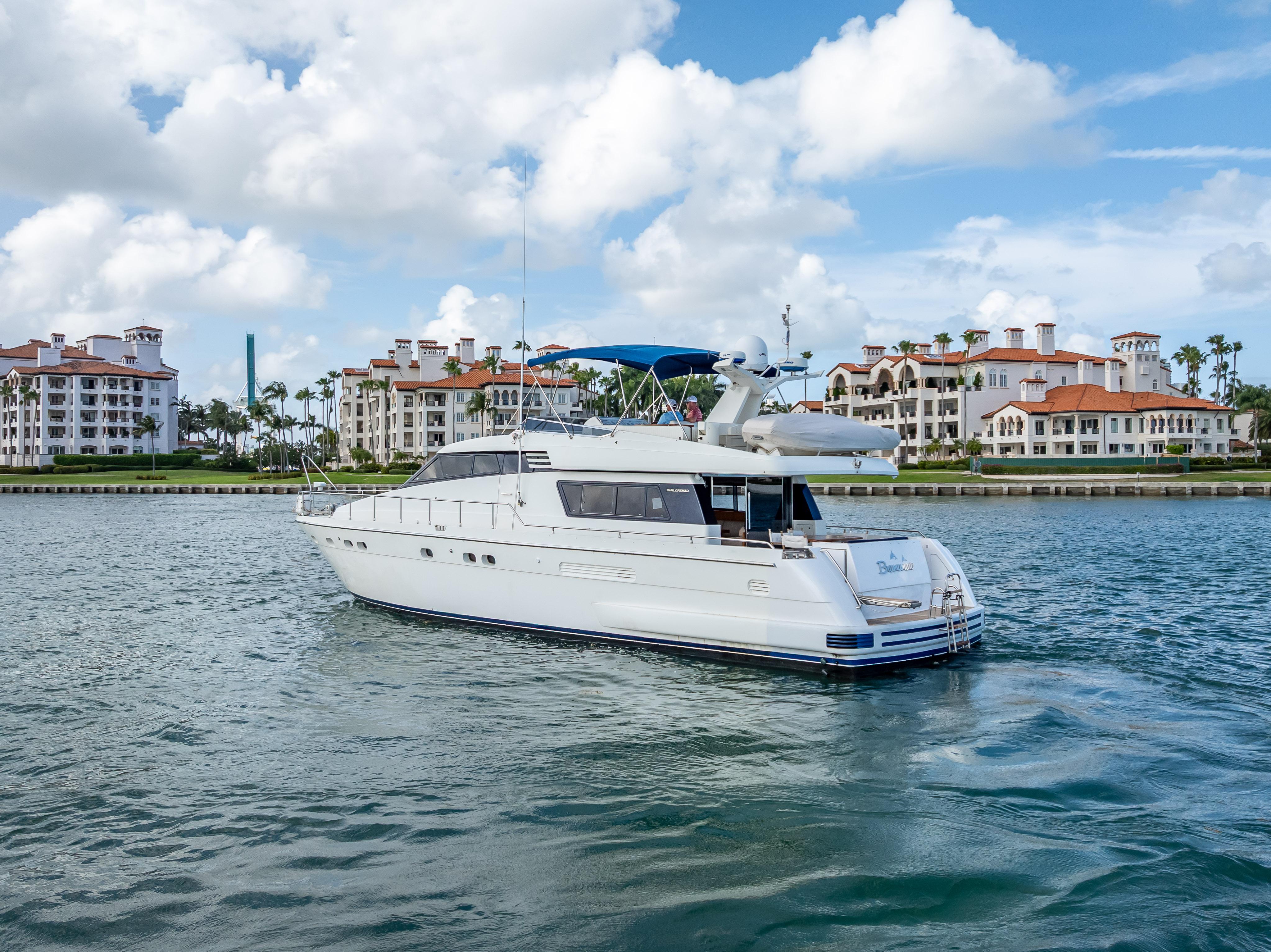 Sanlorenzo 62 yacht from 1995 cruising near waterfront buildings under a cloudy sky.