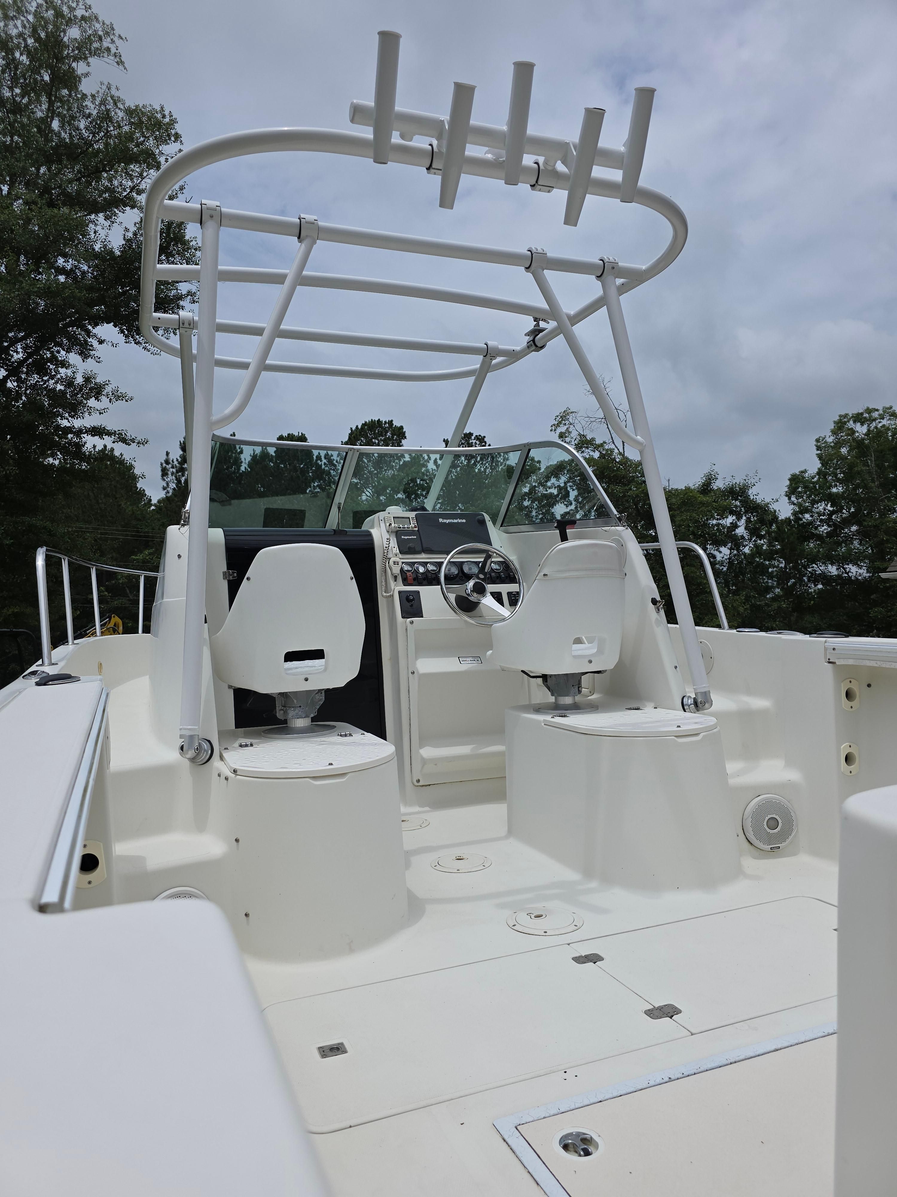 The image shows the cockpit of a 2005 Caravelle Sea Hawk 230 Walk Around OB. It features two white seats and a helm with a glass windshield. A T-top is also visible.