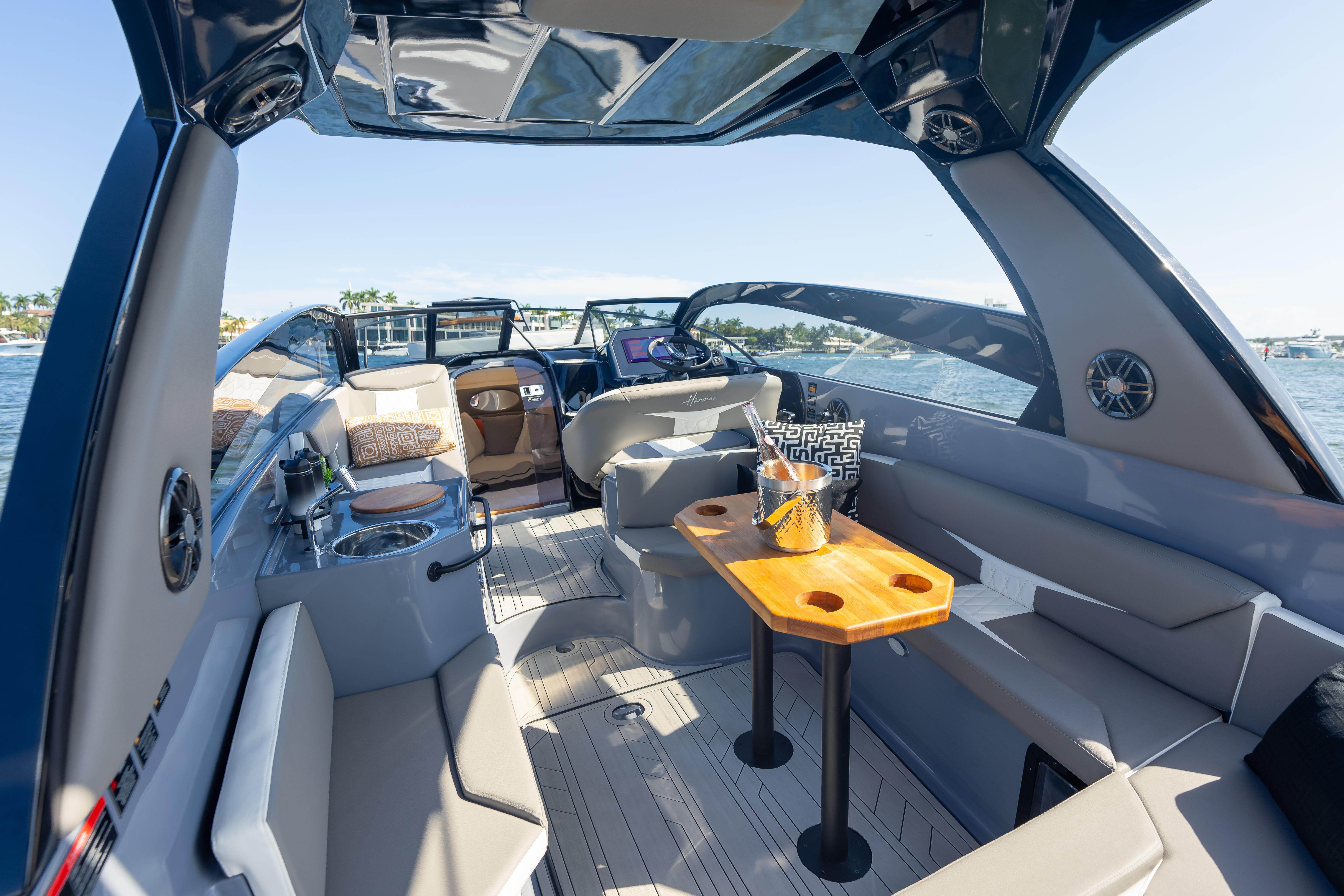 Luxurious 2026 Hanover 305 boat interior with seating, table, and helm, on a sunny day.