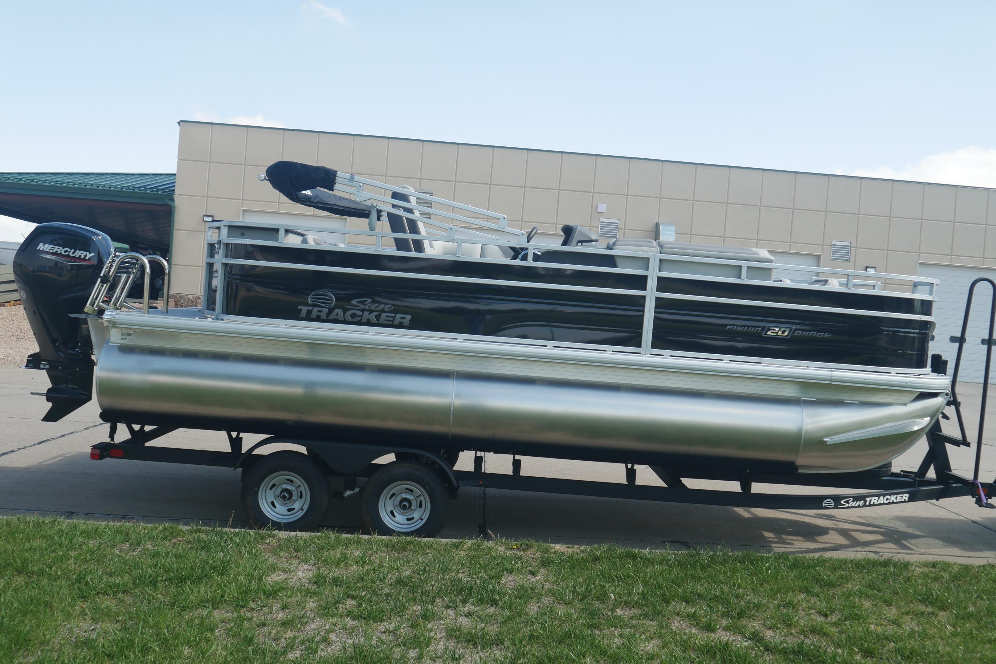 2026 Sun Tracker Fishin' Barge 20 DLX pontoon boat on trailer, parked outdoors.