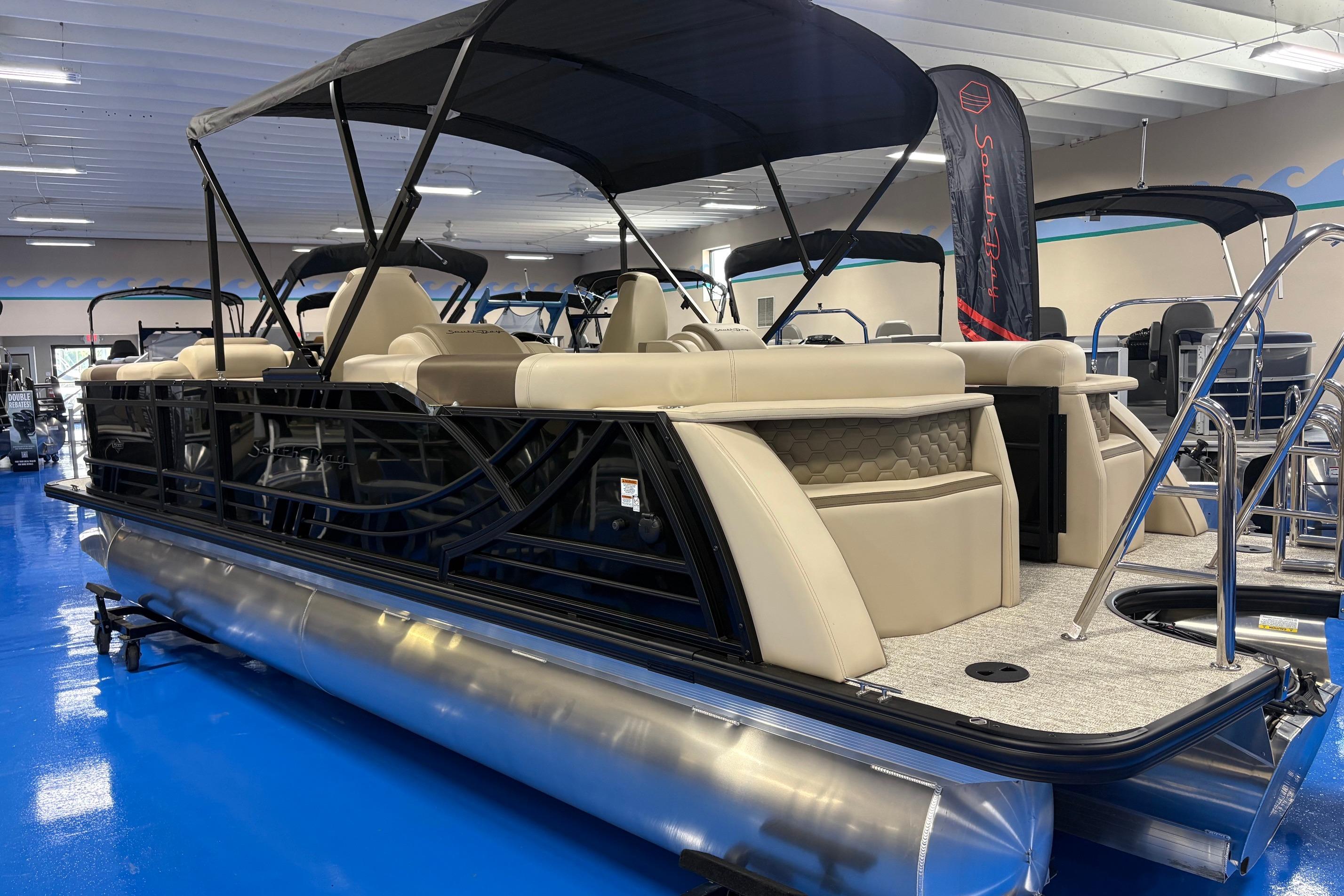 2026 South Bay 523RS pontoon boat with beige seating and black frame in showroom.