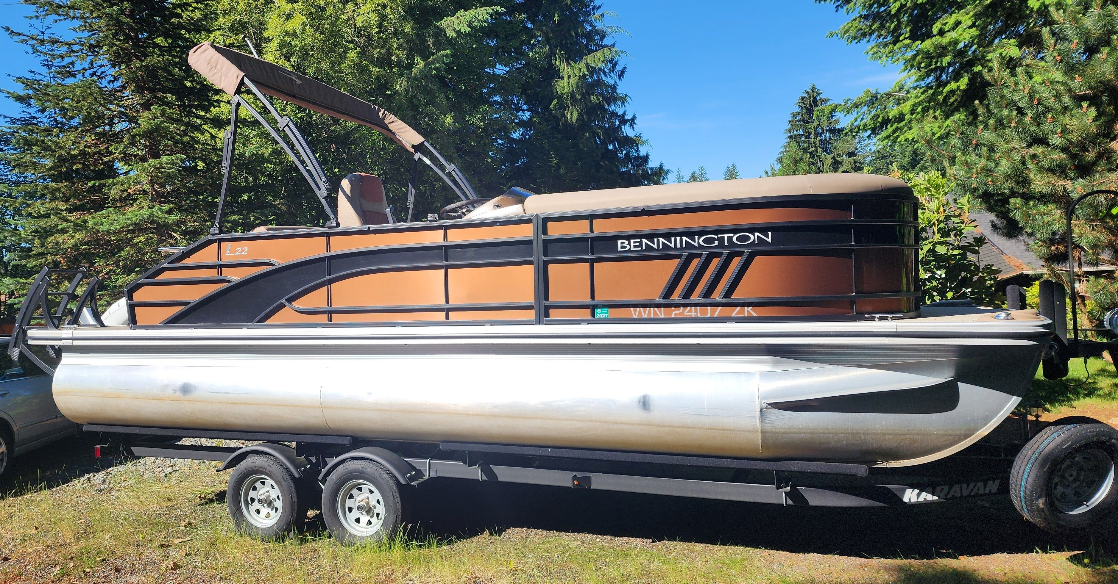 A 2023 Bennington 22 LSB pontoon boat on a trailer, surrounded by trees.