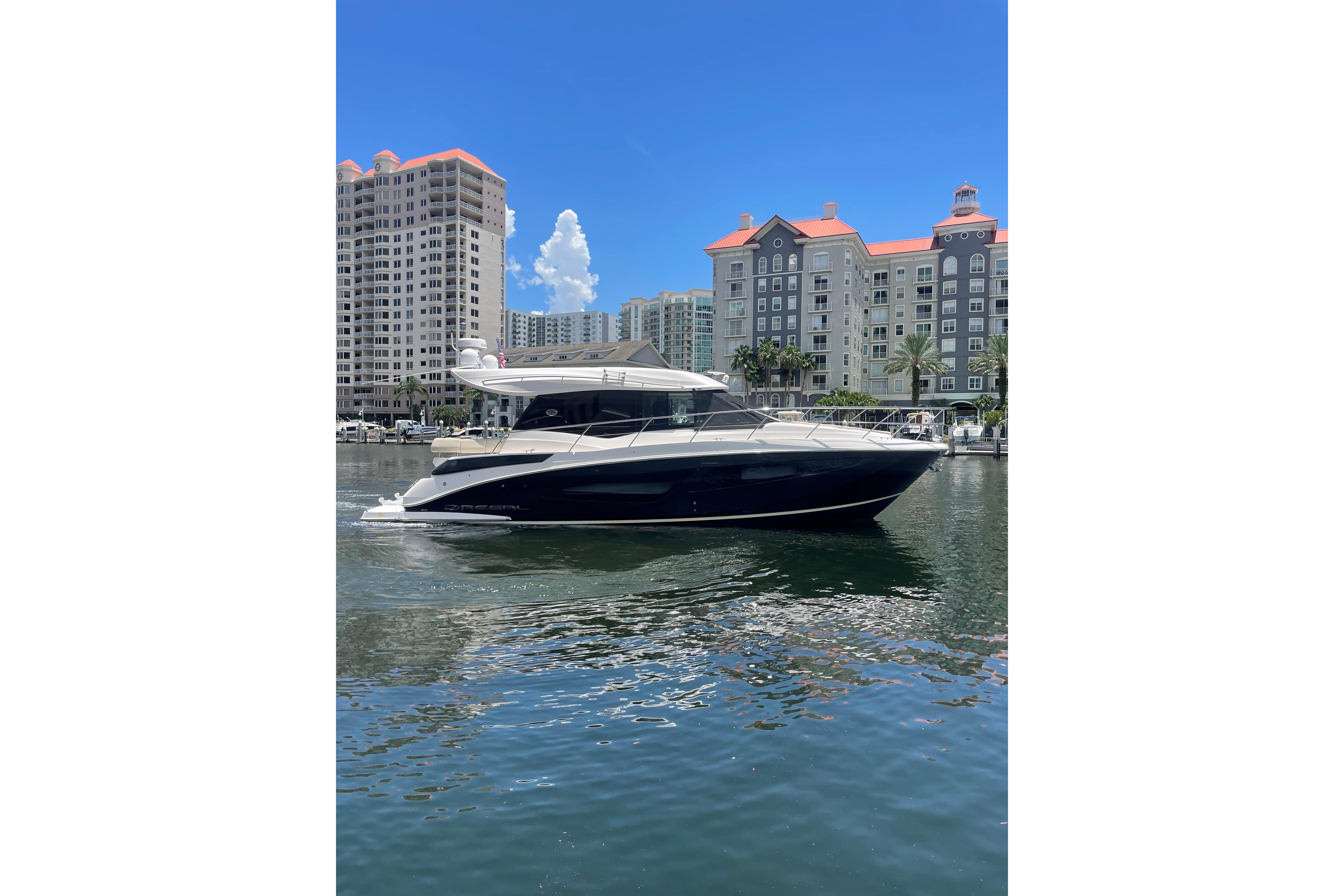 2020 Regal 42 Grande Coupe yacht cruising near waterfront buildings under clear blue sky.