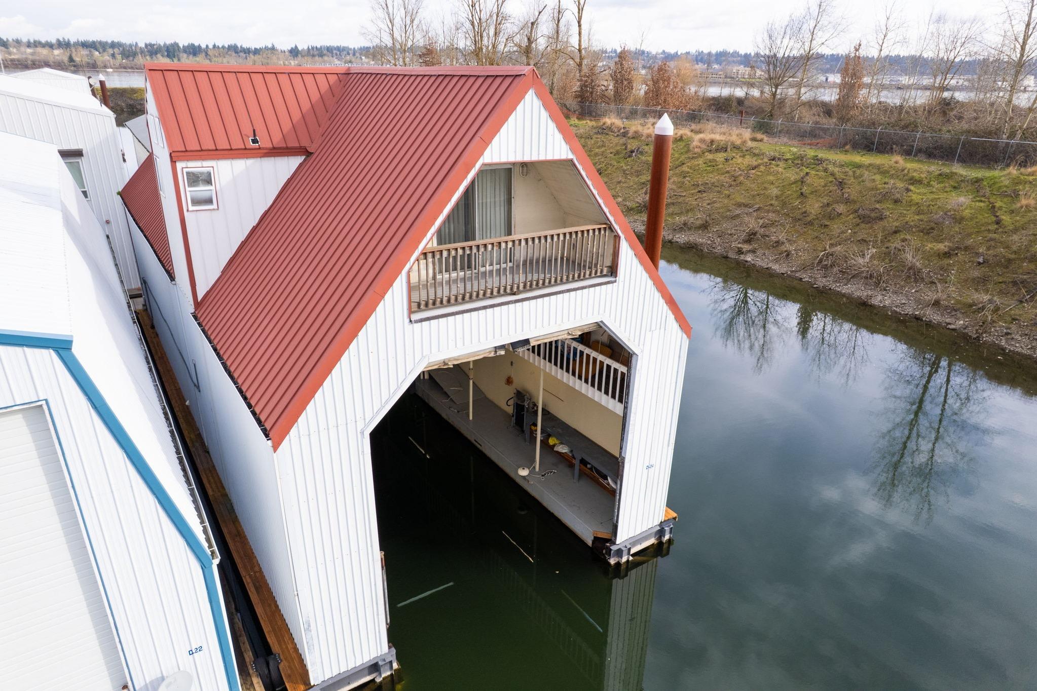 Custom 1976 boathouse with red roof, docked on calm water, surrounded by trees.
