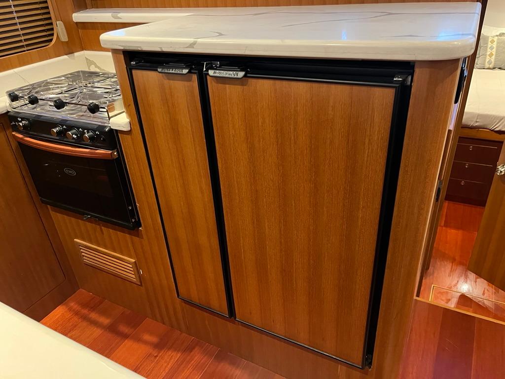 Compact kitchen area in 2025 Bracewell 41 boat with stove and wooden cabinetry.