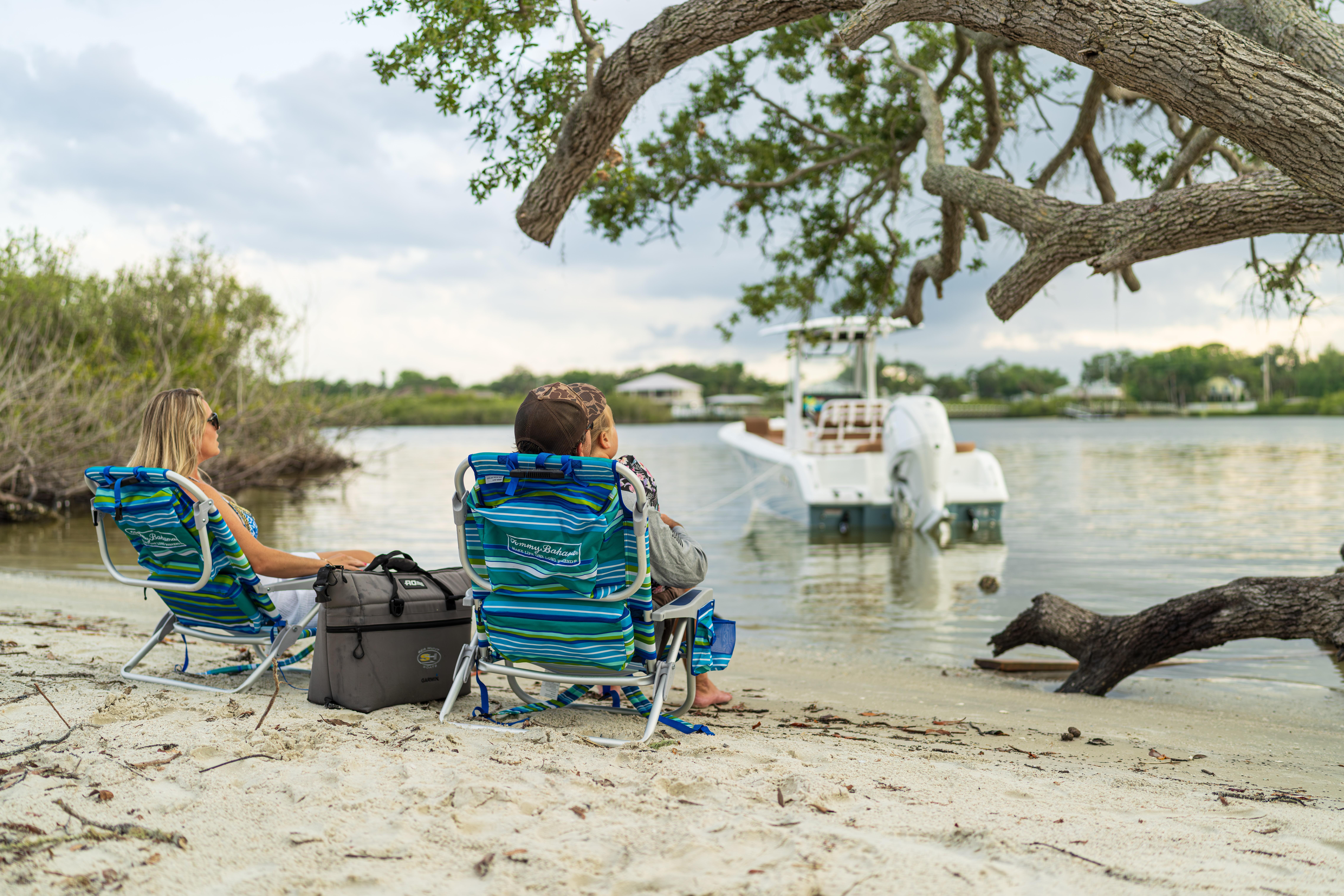 People relaxing on a sandy beach with a 2026 Sea Hunt Ultra 235 SE boat nearby.