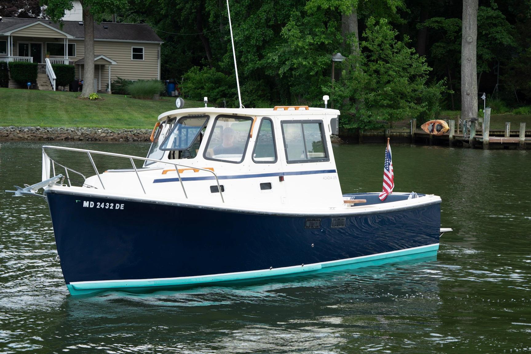 2006 Atlas Boat Works Acadia 25 cruising on a serene lake near a wooded shoreline.