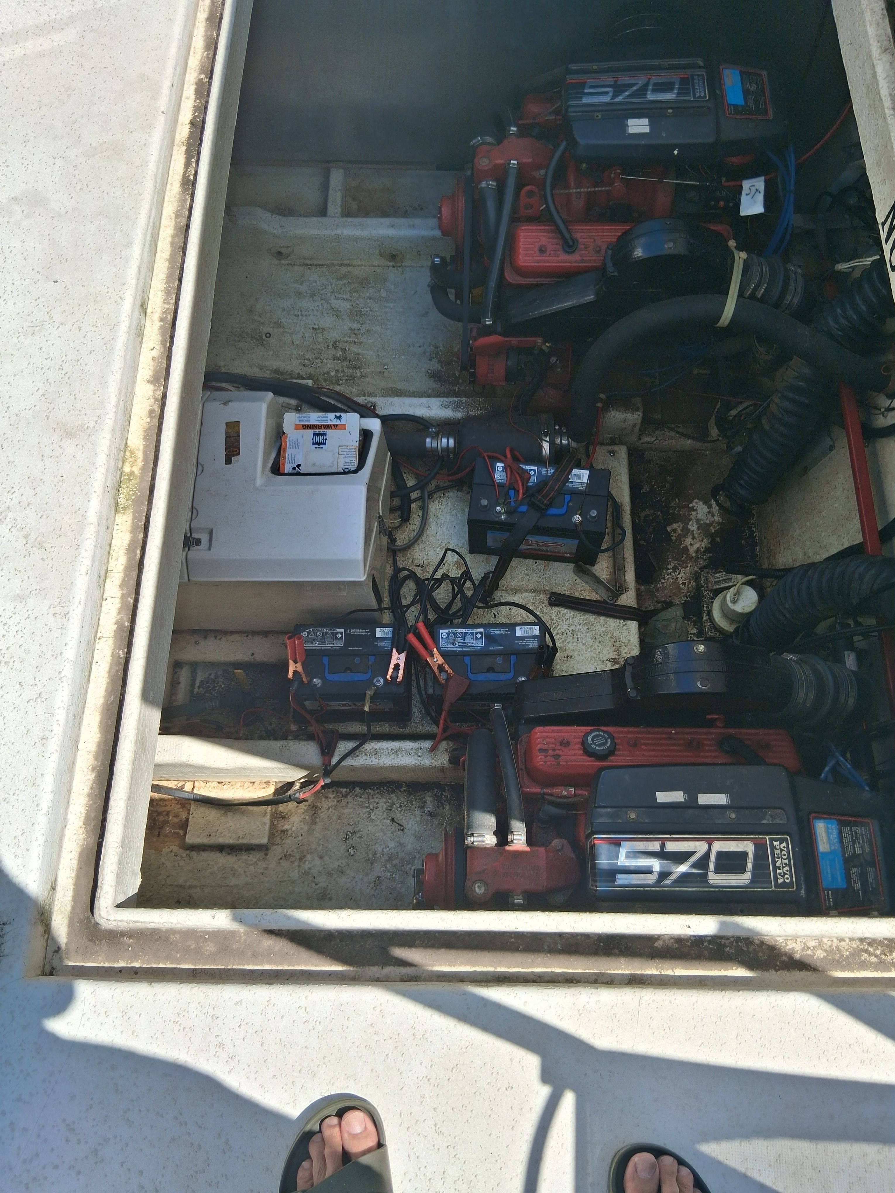 An open engine compartment of a boat showing two engines and several batteries.