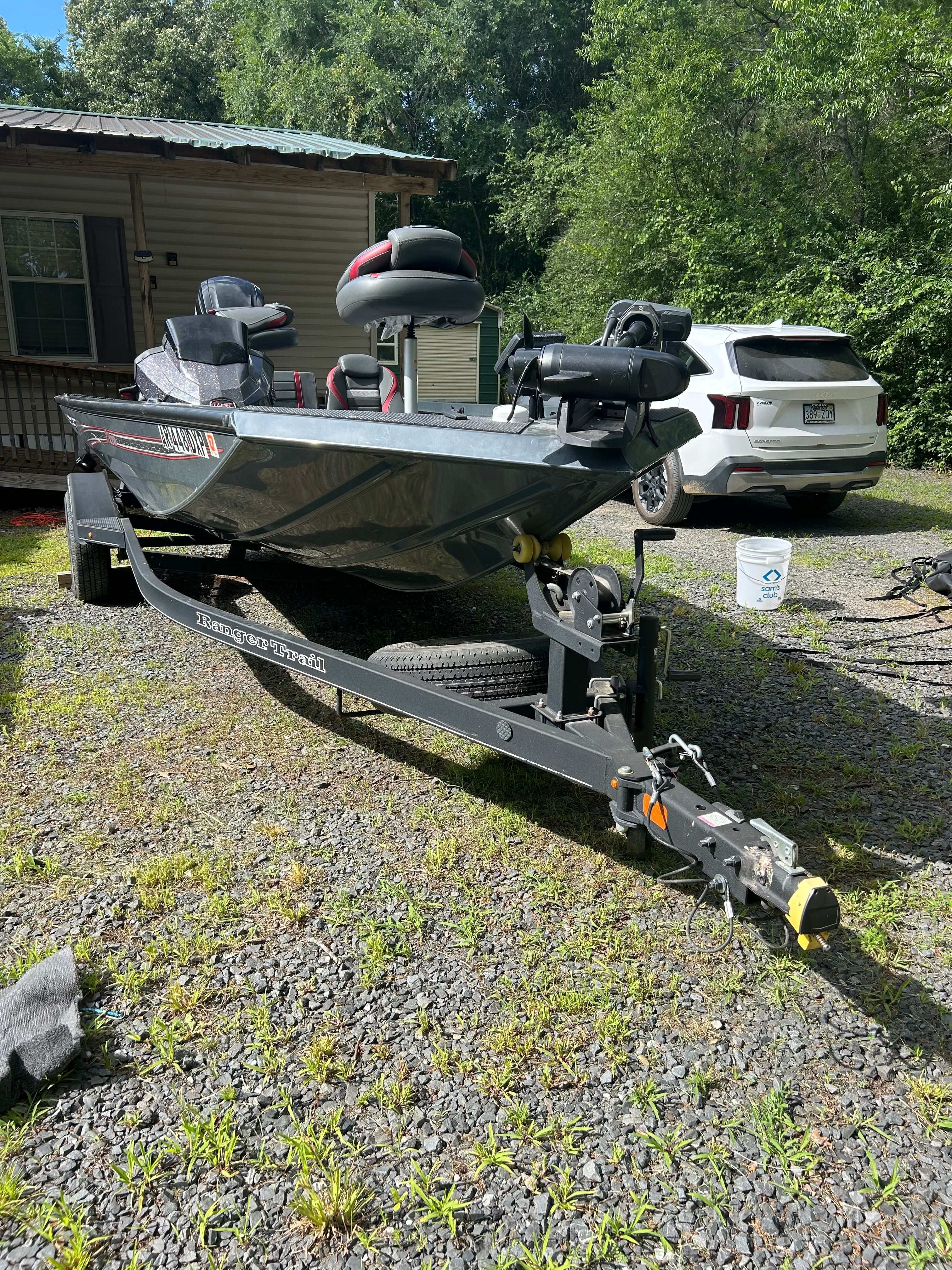 A Ranger RT178 boat on a trailer, parked on a gravel path next to a house.