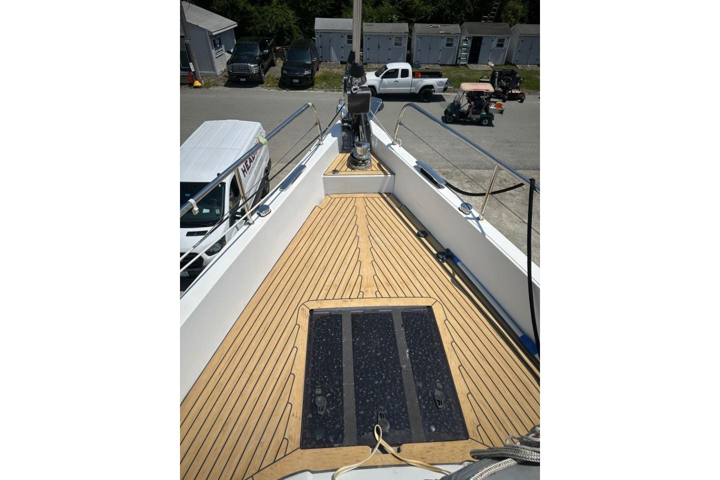 Deck view of 2019 Moody 54 DS yacht with wooden flooring and docked vehicles nearby.