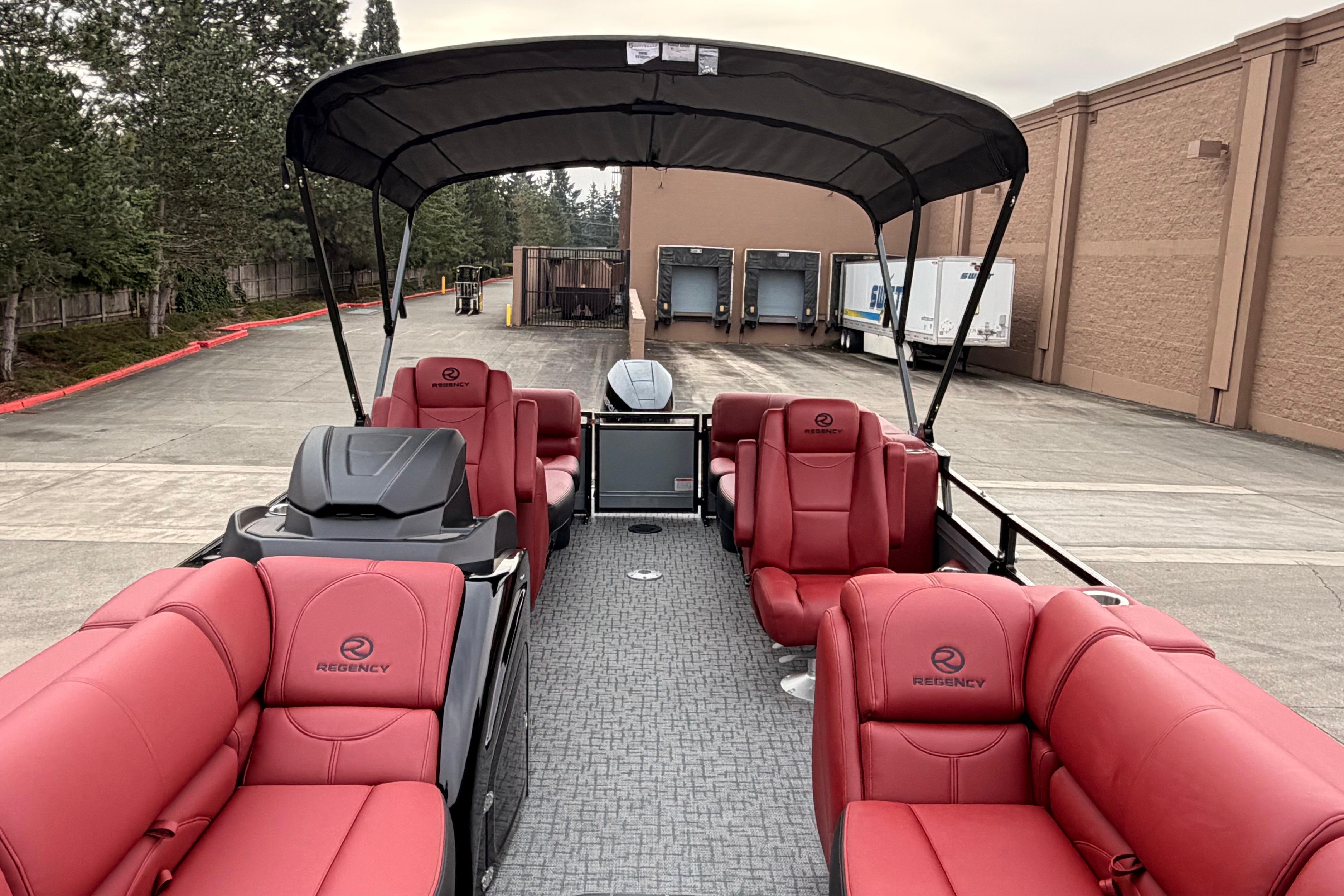 2026 Regency 250 DL pontoon boat with red seating and canopy in a parking area.