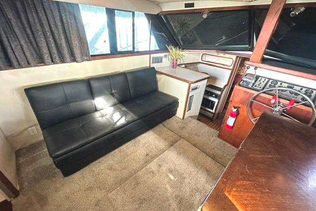 Interior of 1989 Carver 32 Aft Cabin Motor Yacht with black sofa and helm.