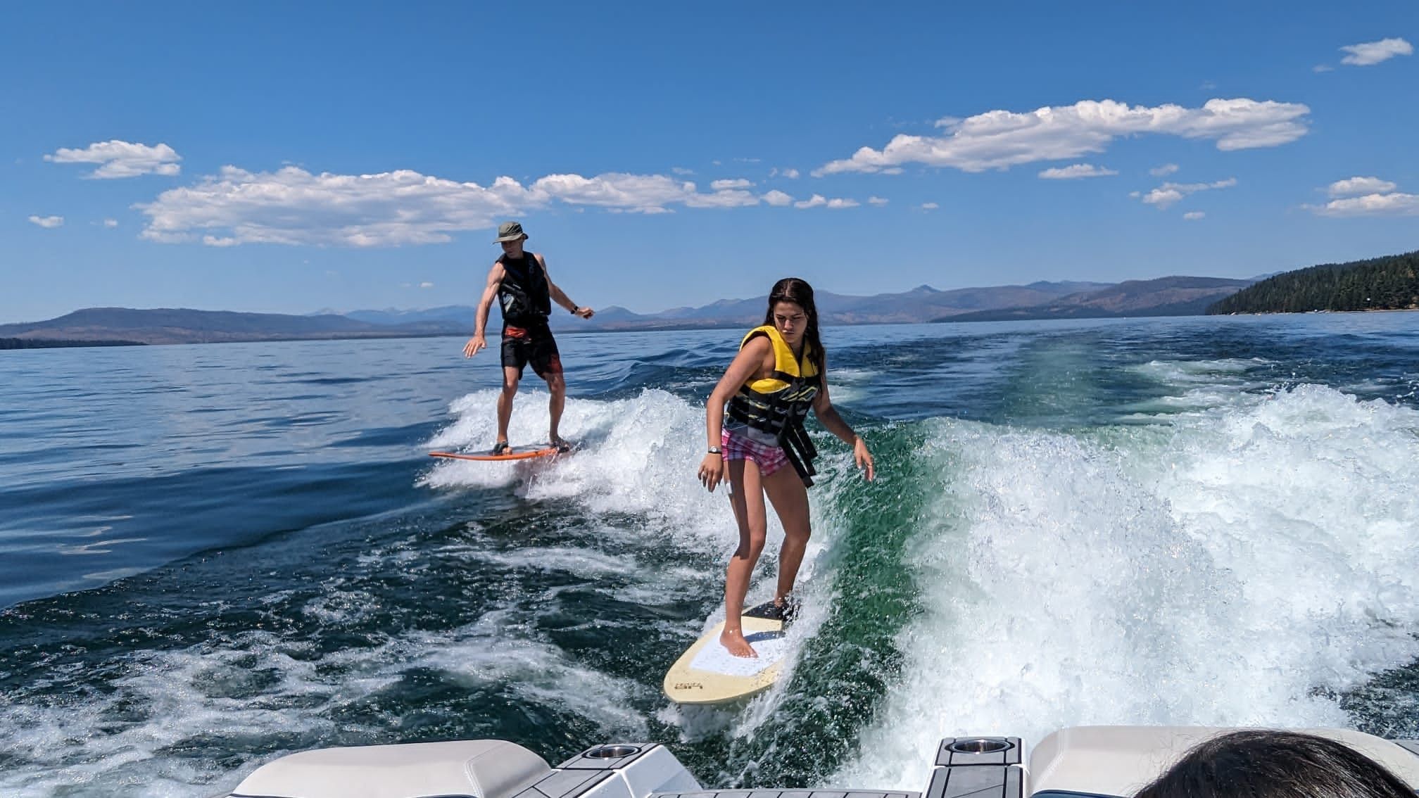 Two people surfing behind a Nautique boat on a lake.
