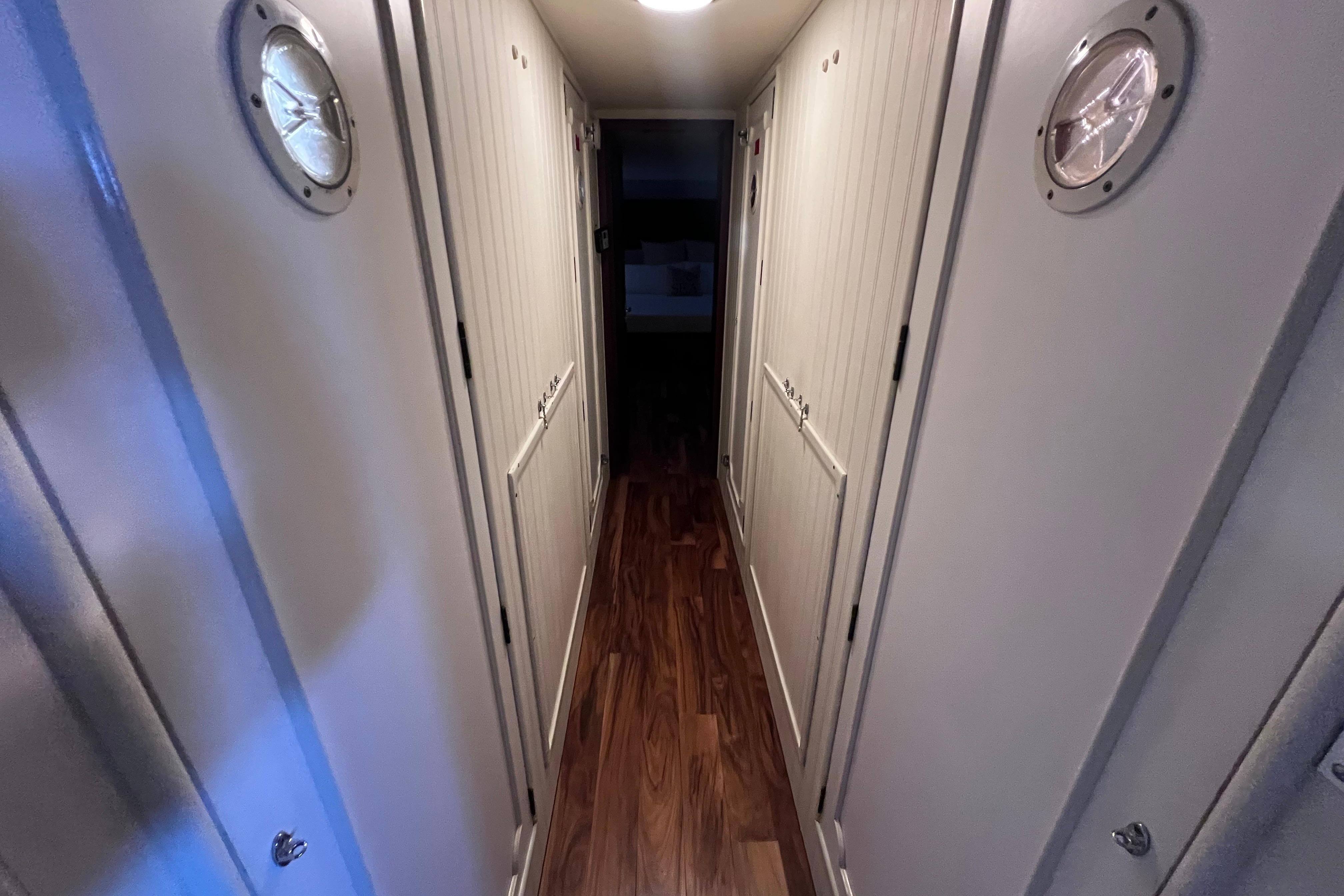 Narrow hallway inside 1987 Hatteras 70 Cockpit Motor Yacht with wooden flooring and porthole windows.