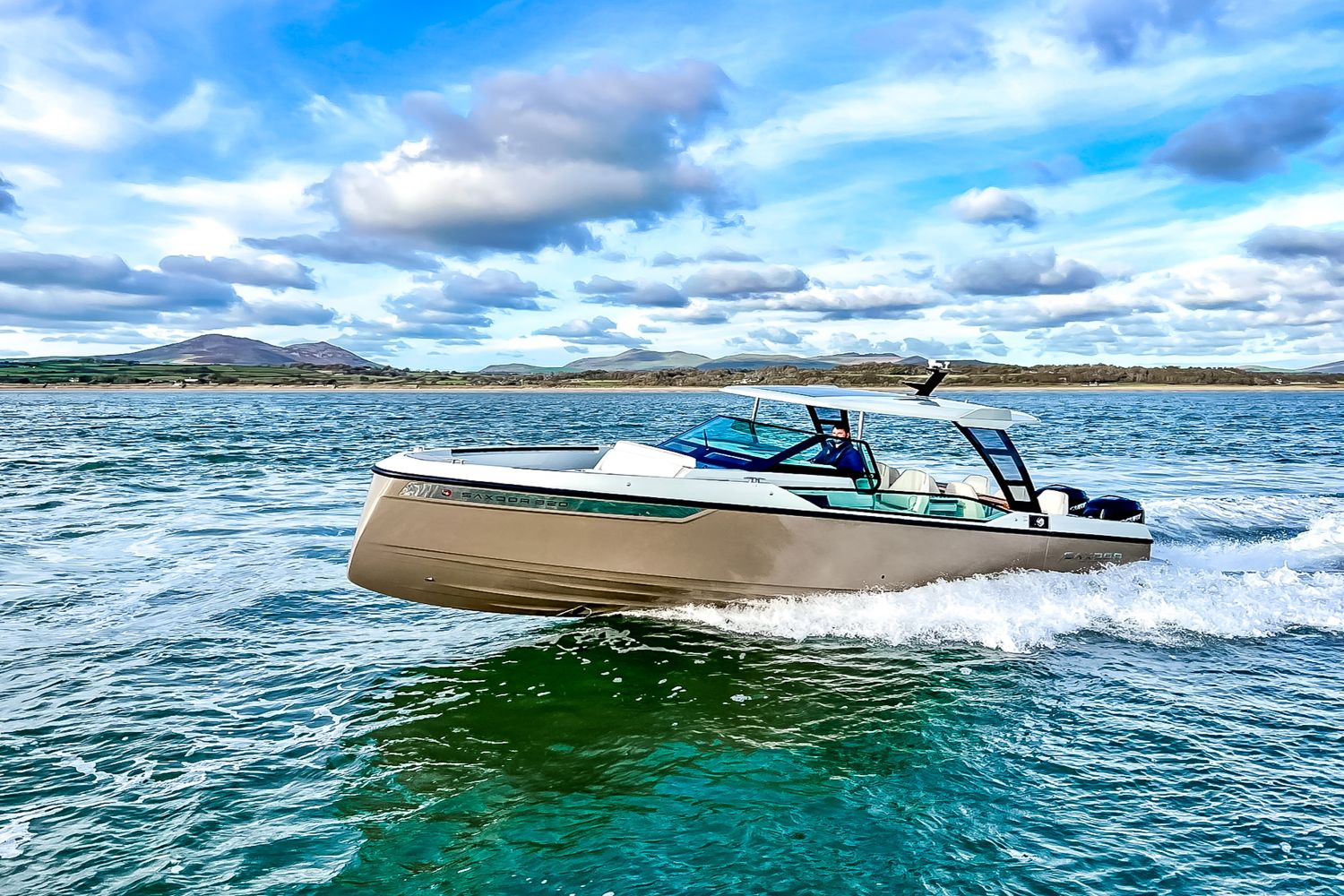 A modern motorboat speeds across the water under a blue sky with clouds.