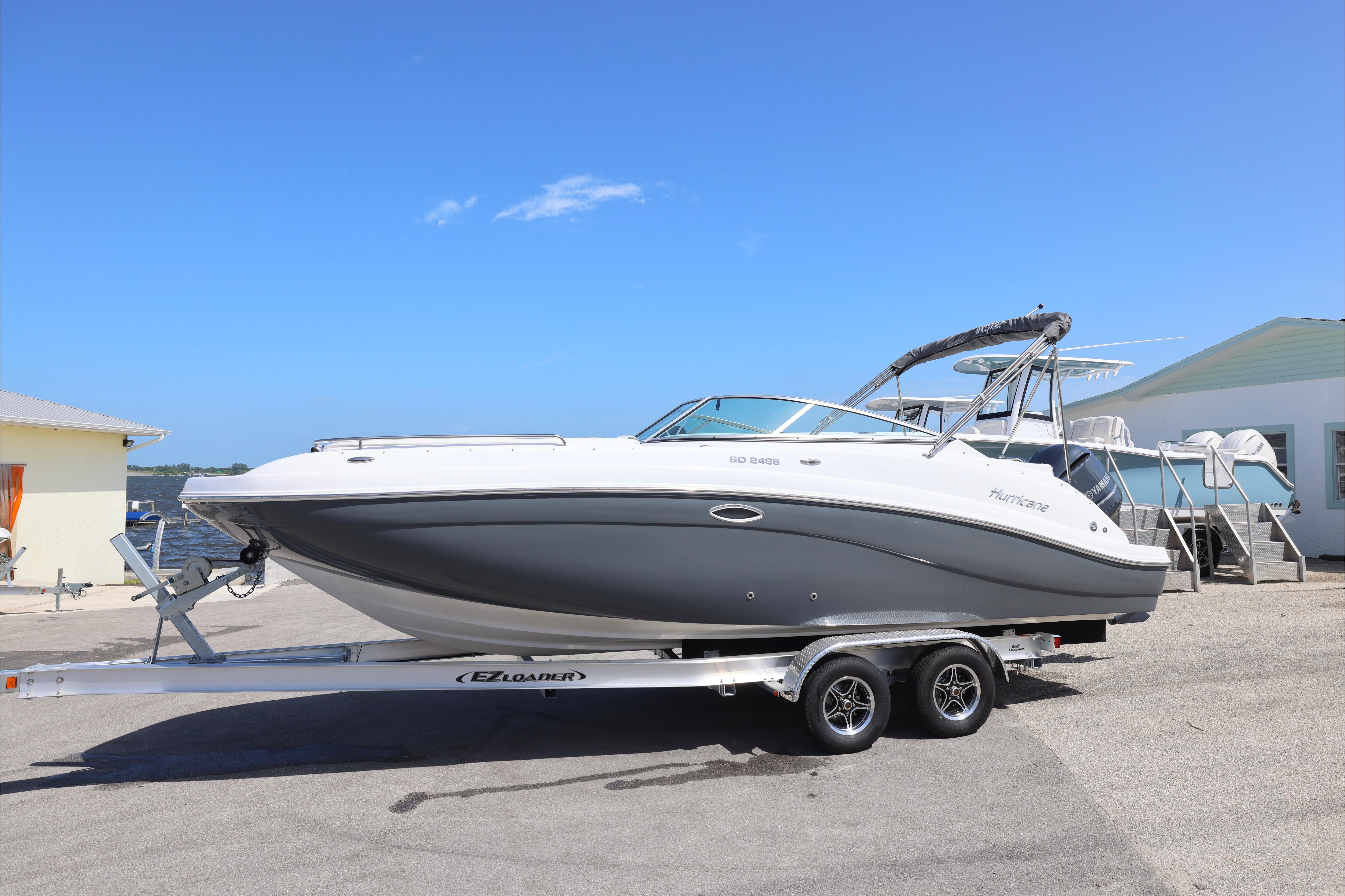 2026 Hurricane SunDeck 2486 OB boat on trailer, parked outdoors under clear blue sky.