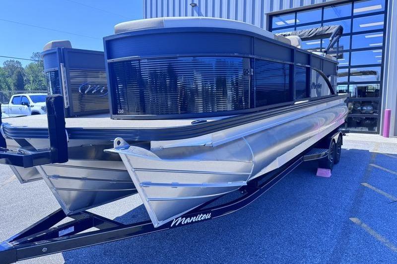 2027 Manitou Aurora 23 RF SHP pontoon boat on trailer outside a building.