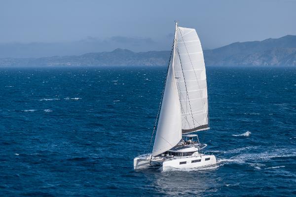 2025 Lagoon 51 ICONIC catamaran sailing on open sea with mountainous backdrop.