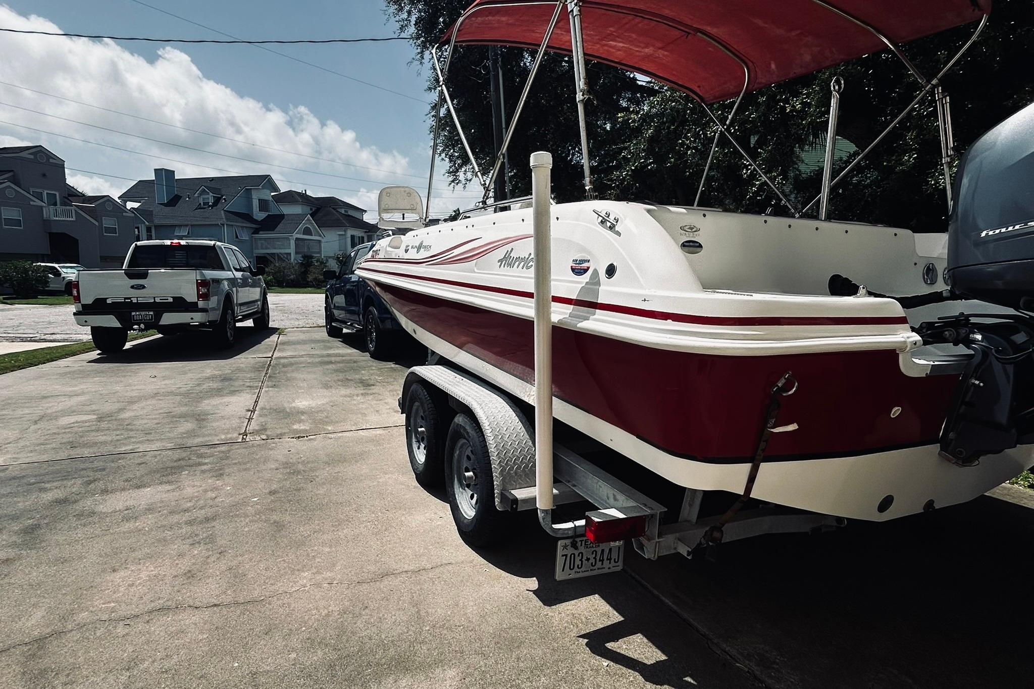 2013 Hurricane SunDeck Sport 201 OB boat on trailer, parked in driveway with red canopy.