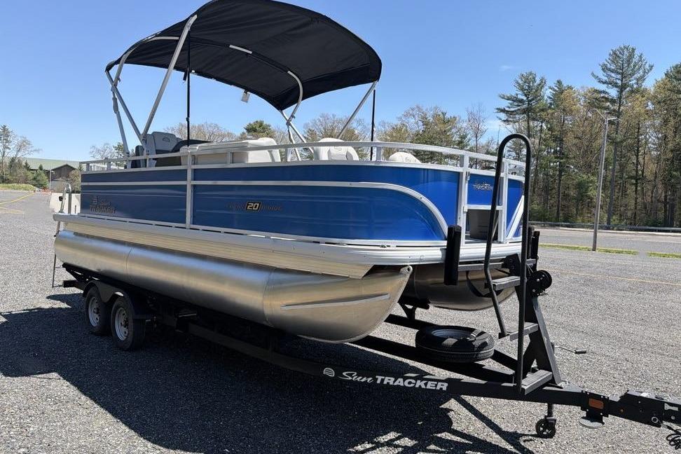 2026 Sun Tracker Fishin' Barge 20 DLX pontoon boat on trailer, parked outdoors.