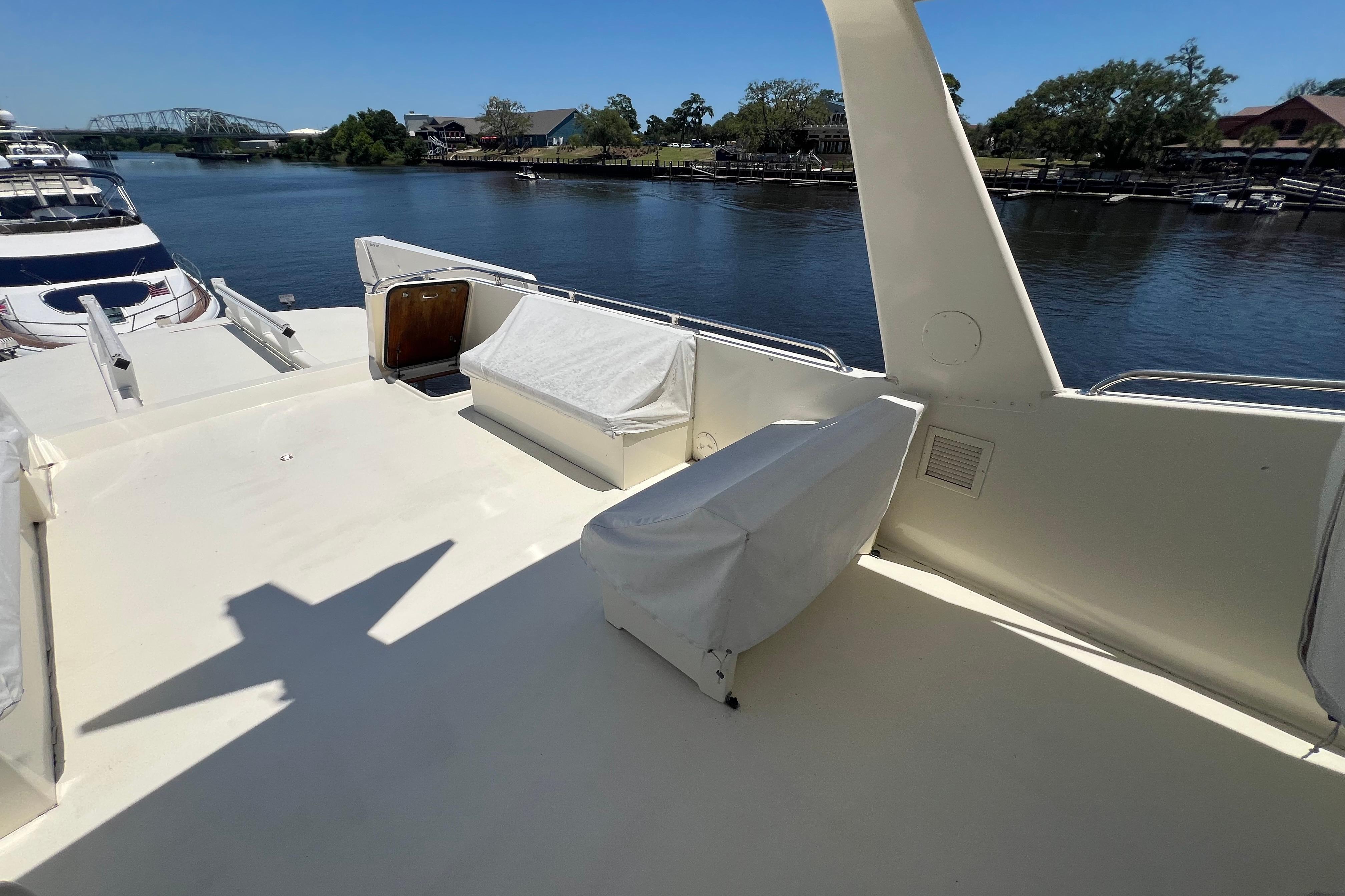 1987 Hatteras 70 Cockpit Motor Yacht deck with covered seating, docked by a scenic river.