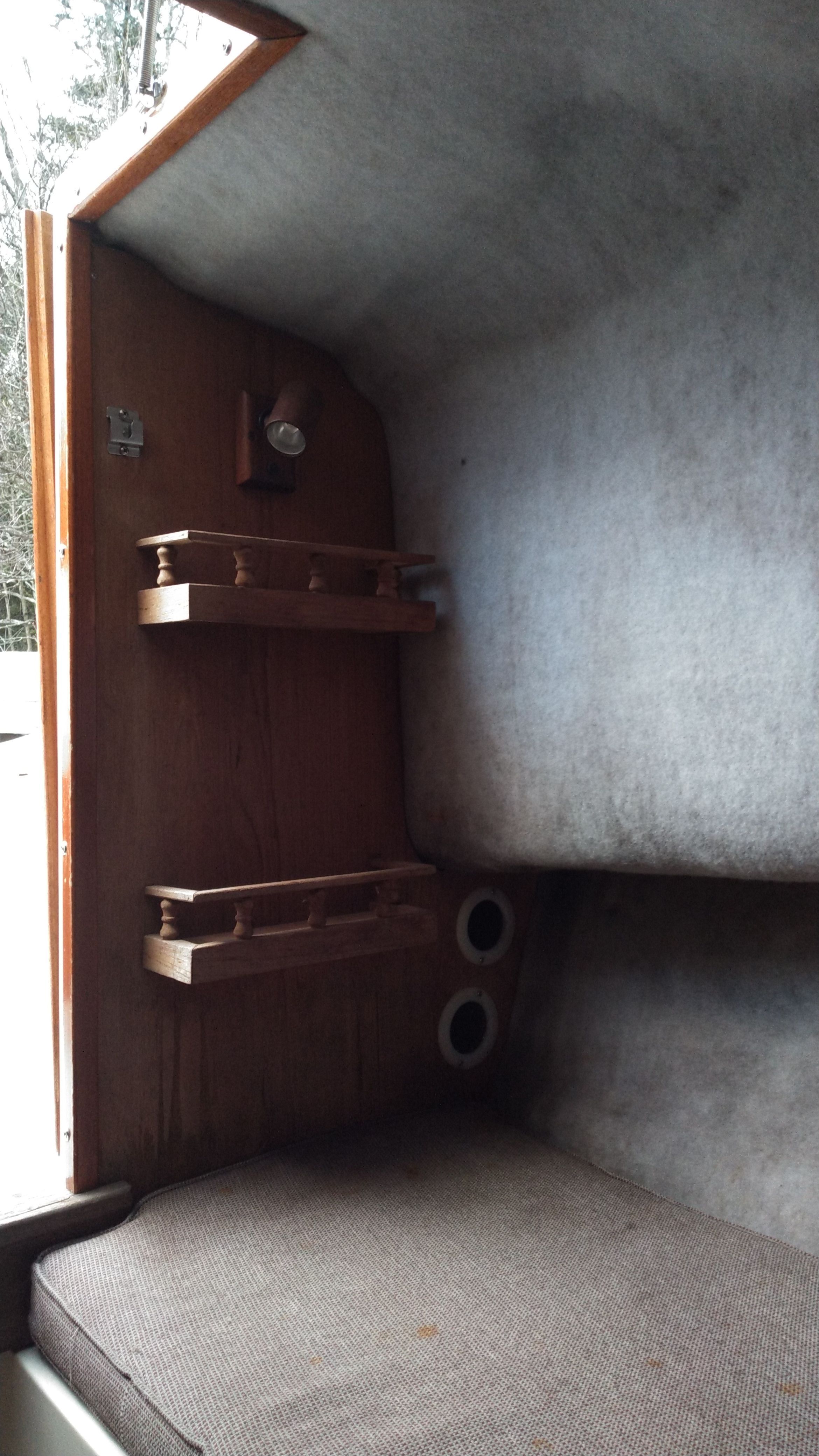 Interior of a boat with gray upholstery and wooden shelves.