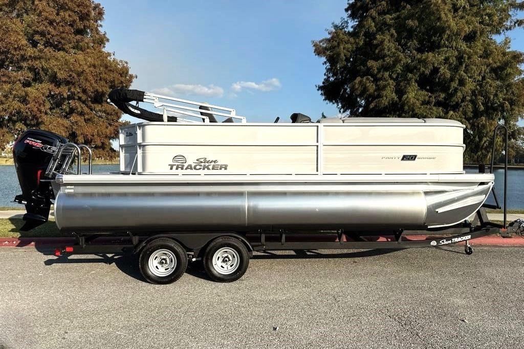2026 Sun Tracker Party Barge 20 DLX pontoon boat on trailer by a lake.
