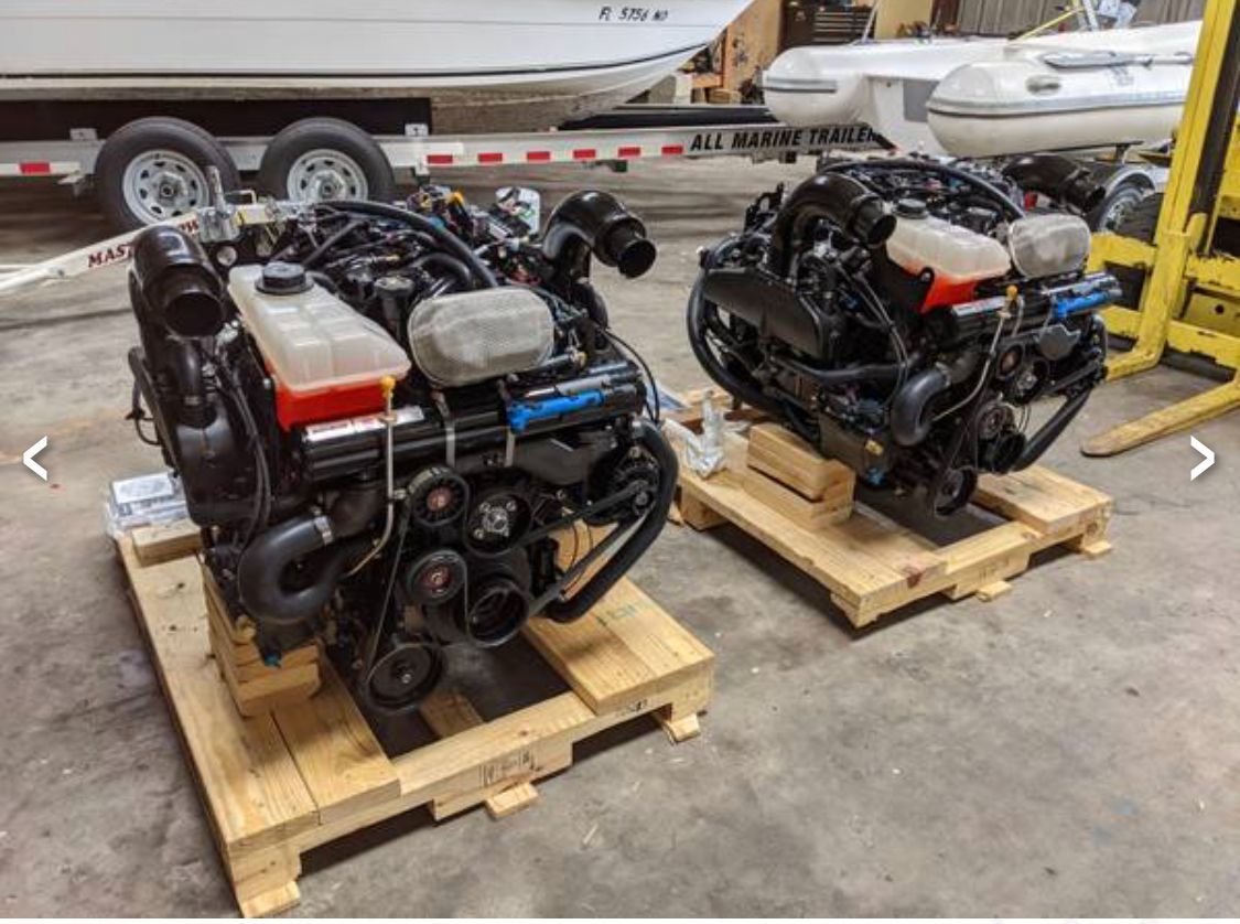 Two engines on wooden pallets in a workshop, with a boat in the background.