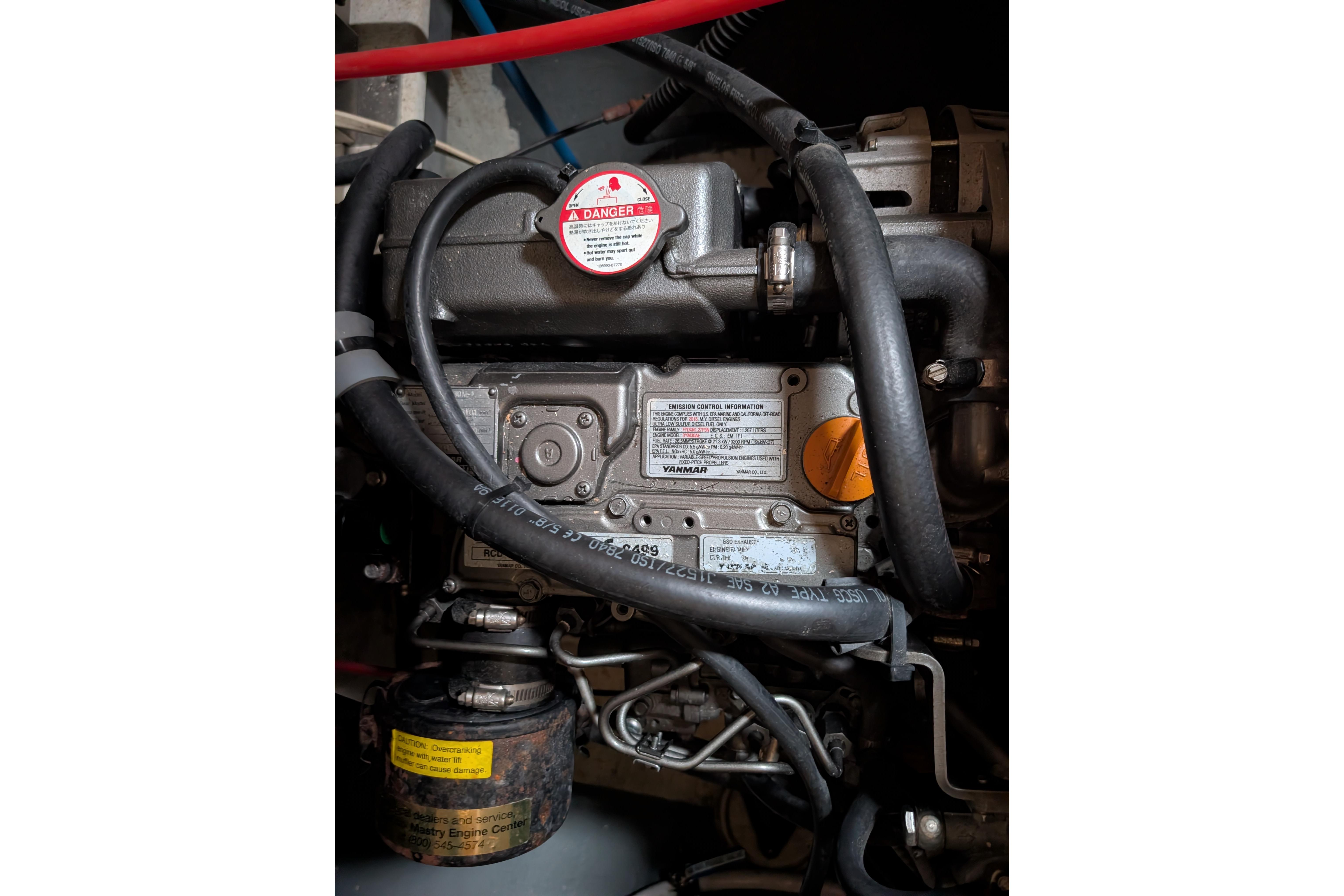 Engine compartment of a 1999 Island Spirit 37 sailboat, featuring hoses and warning labels.