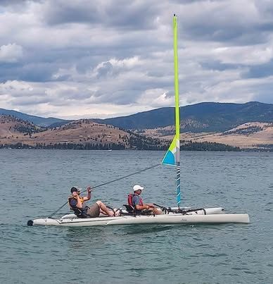 Two people sailing a Hobie Cat Mirage Tandem Island on a calm lake.