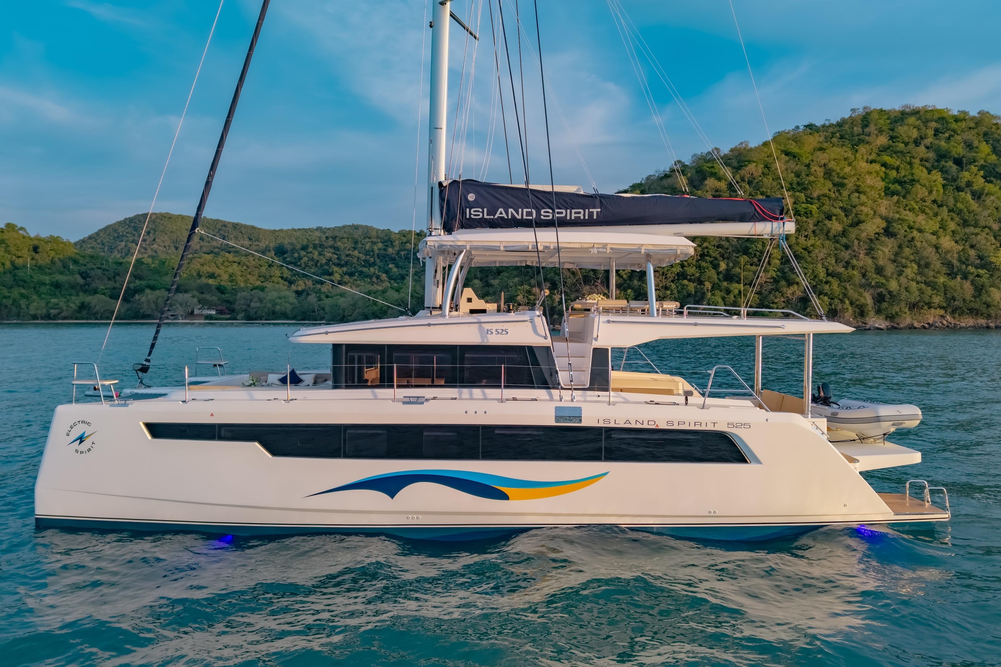 2026 Island Spirit 525E catamaran sailing on serene waters near lush green hills.