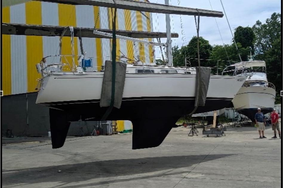 1981 Sabre 30 sailboat suspended in a boatyard with yellow-striped building background.