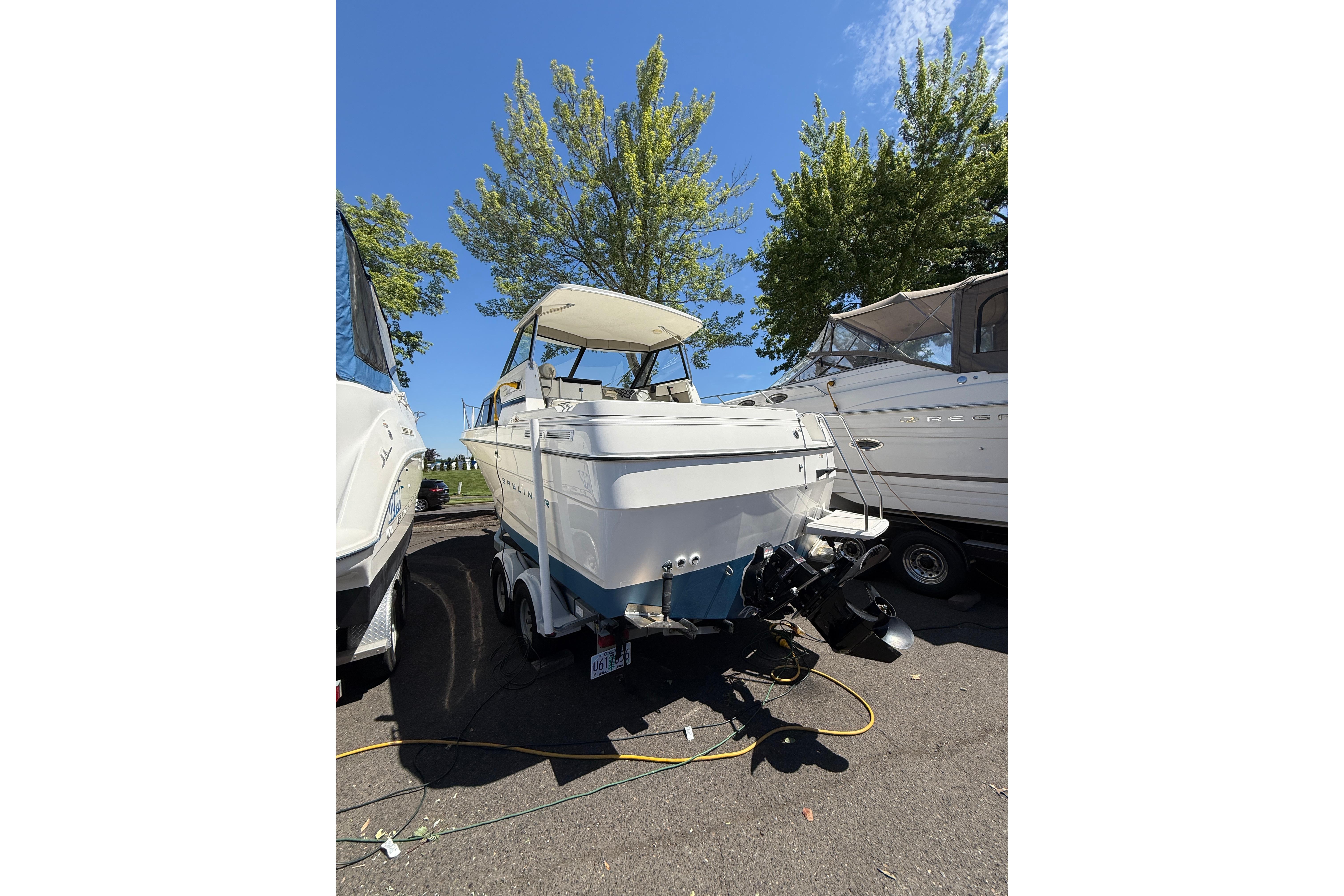 1997 Bayliner 2452 Ciera Express boat on trailer, parked outdoors under clear blue sky.