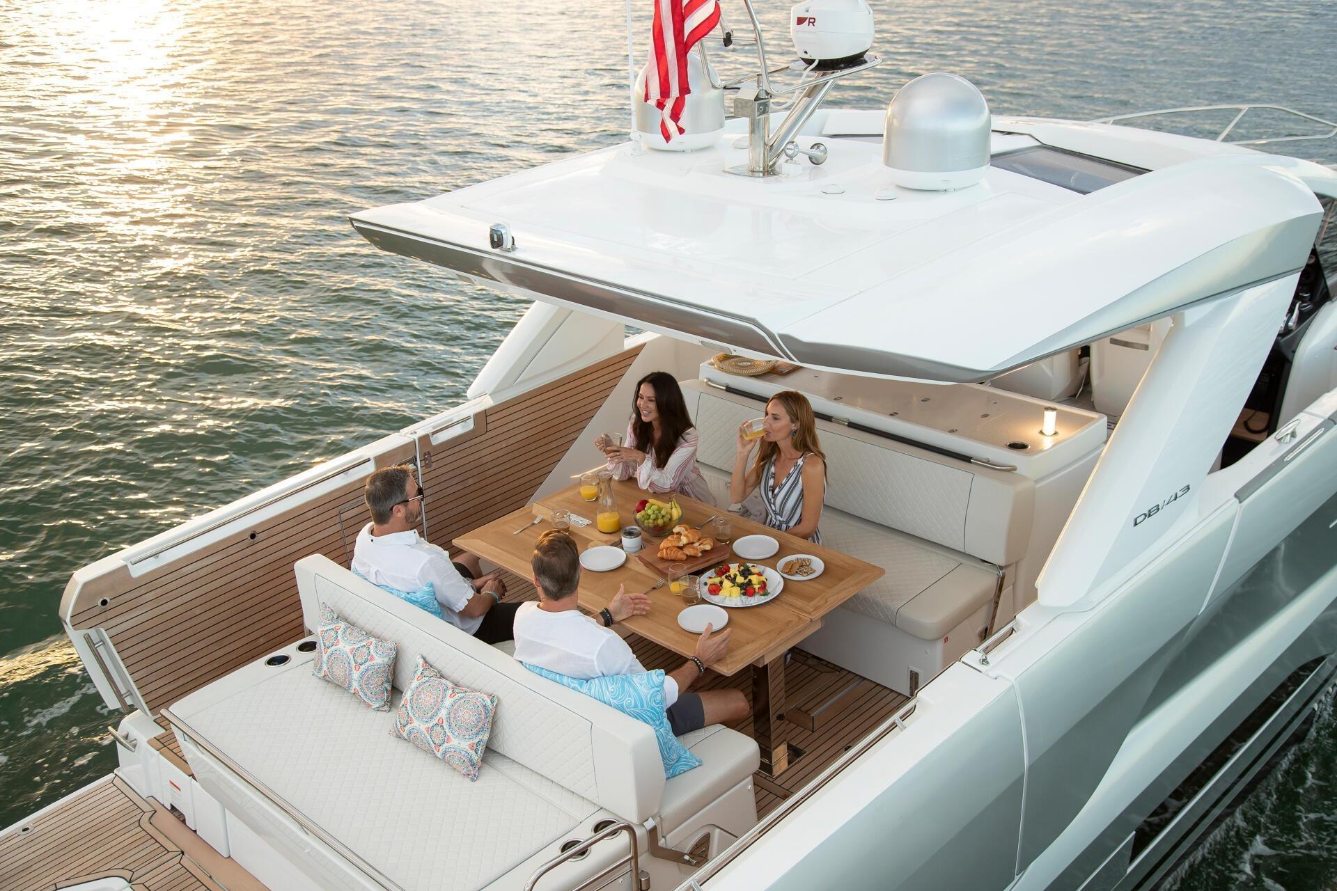 People dining on a 2027 Jeanneau DB/43 OB yacht, enjoying a meal on the water.