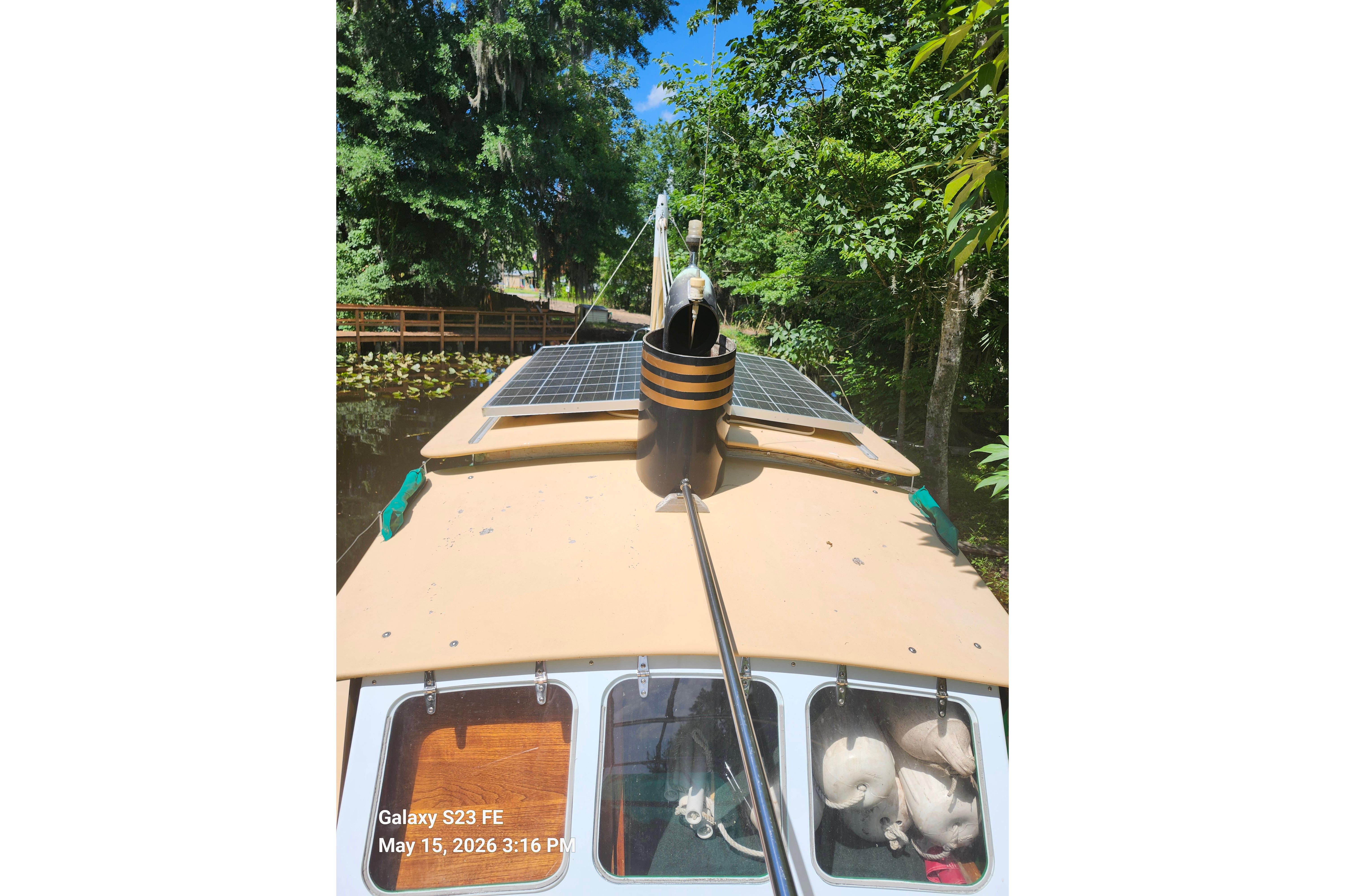 1995 Bonny Rover boat with solar panels cruising through a lush, tree-lined waterway.