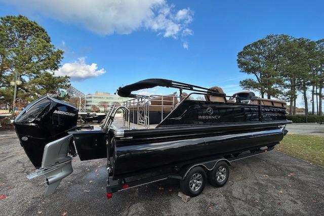 2025 Regency 230 LE3 Sport pontoon boat with Mercury engine on trailer, parked outdoors.