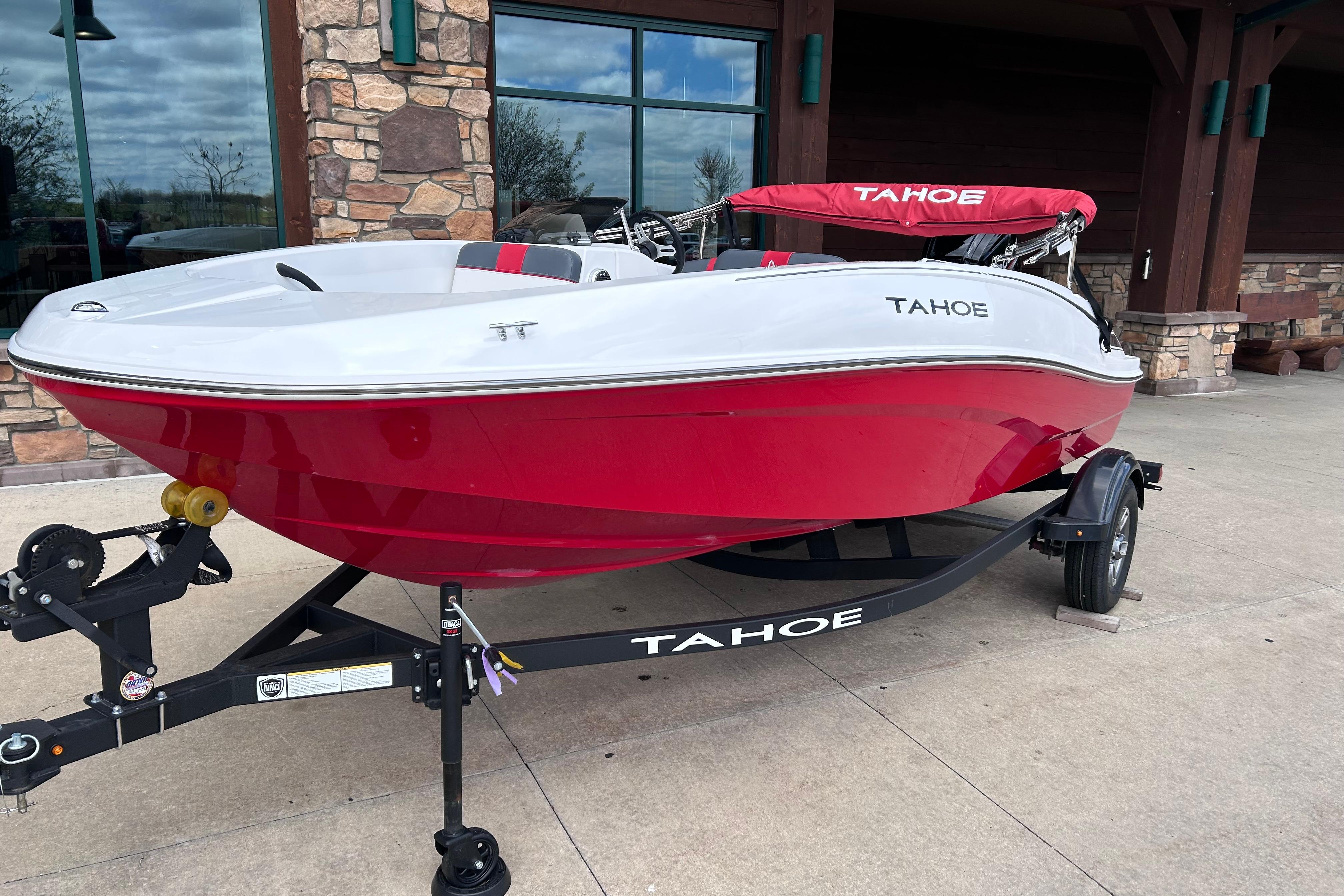 2026 Tahoe T16 boat in red and white on a trailer outside a building.