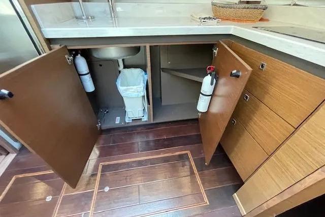 2016 Sea Ray Sundancer 510 yacht kitchen with open cabinets, fire extinguishers, and wooden flooring.