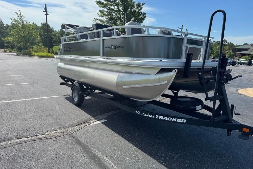 2026 Sun Tracker Bass Buggy 16 XL Select pontoon boat on trailer in parking lot.