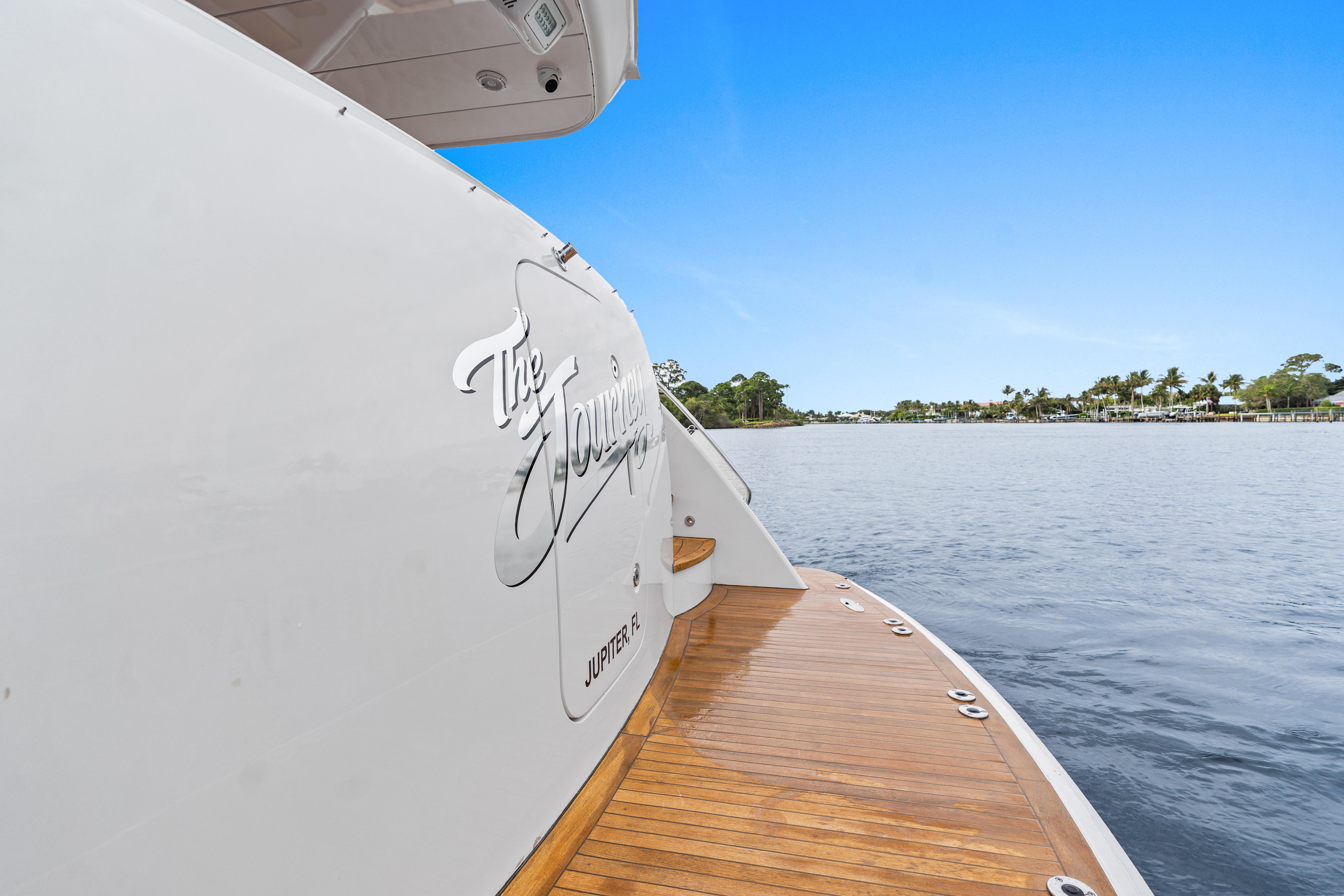2008 Hatteras 64 Motor Yacht on calm water, featuring teak deck and scenic shoreline.
