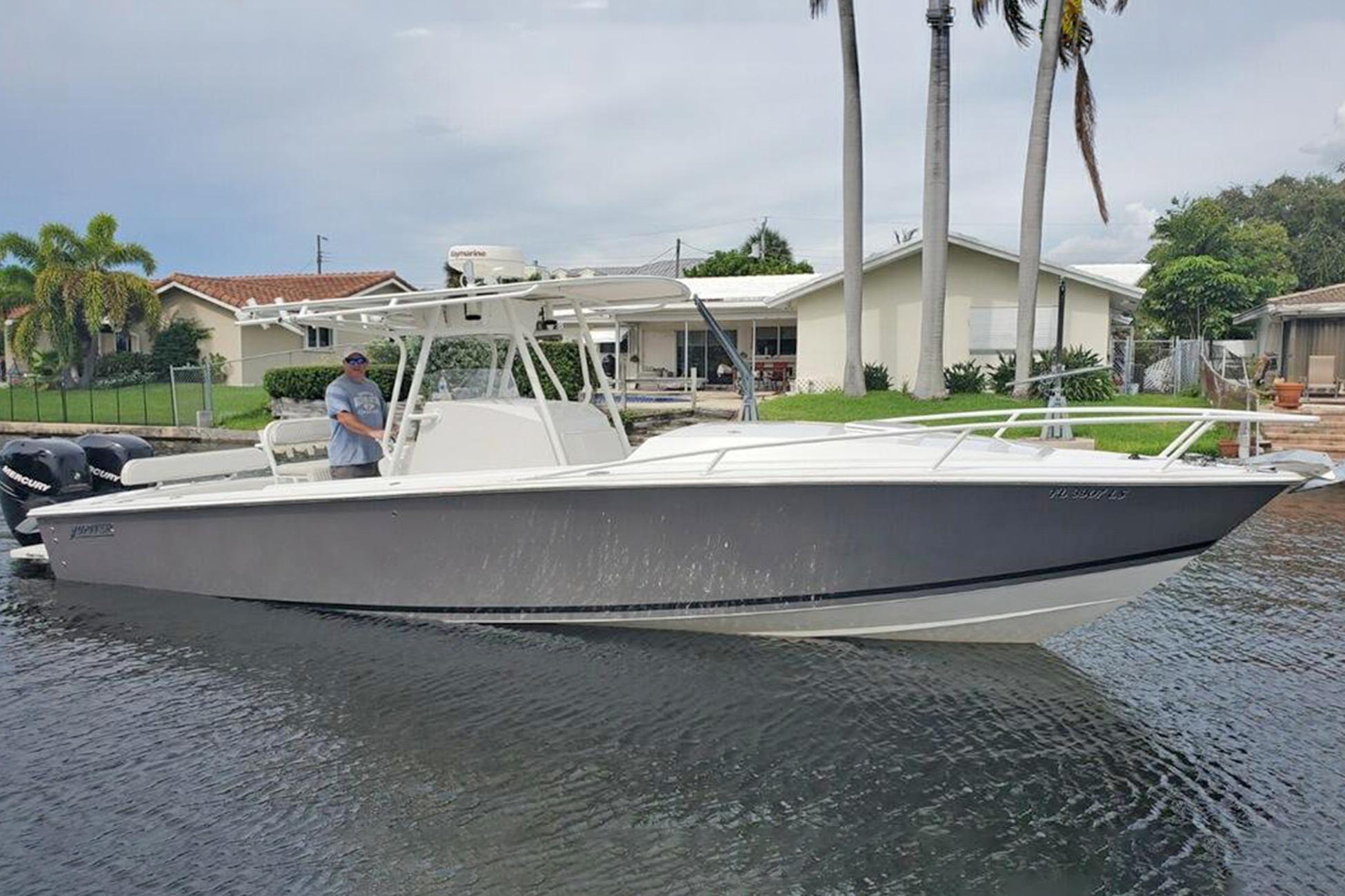 2001 Jupiter 31 Cuddy boat on water, with palm trees and houses in the background.