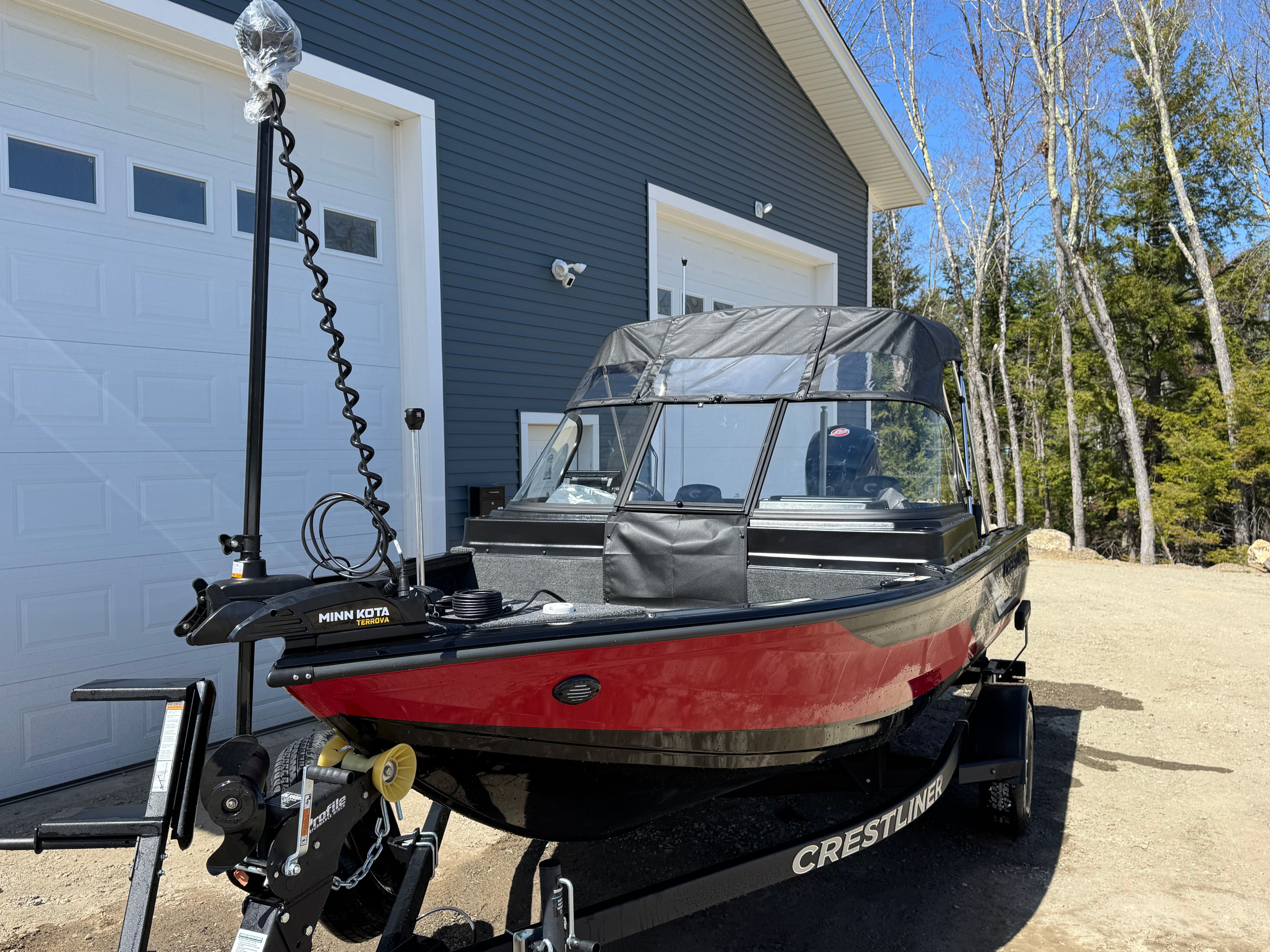 A red Crestliner boat is on a trailer in front of a garage.