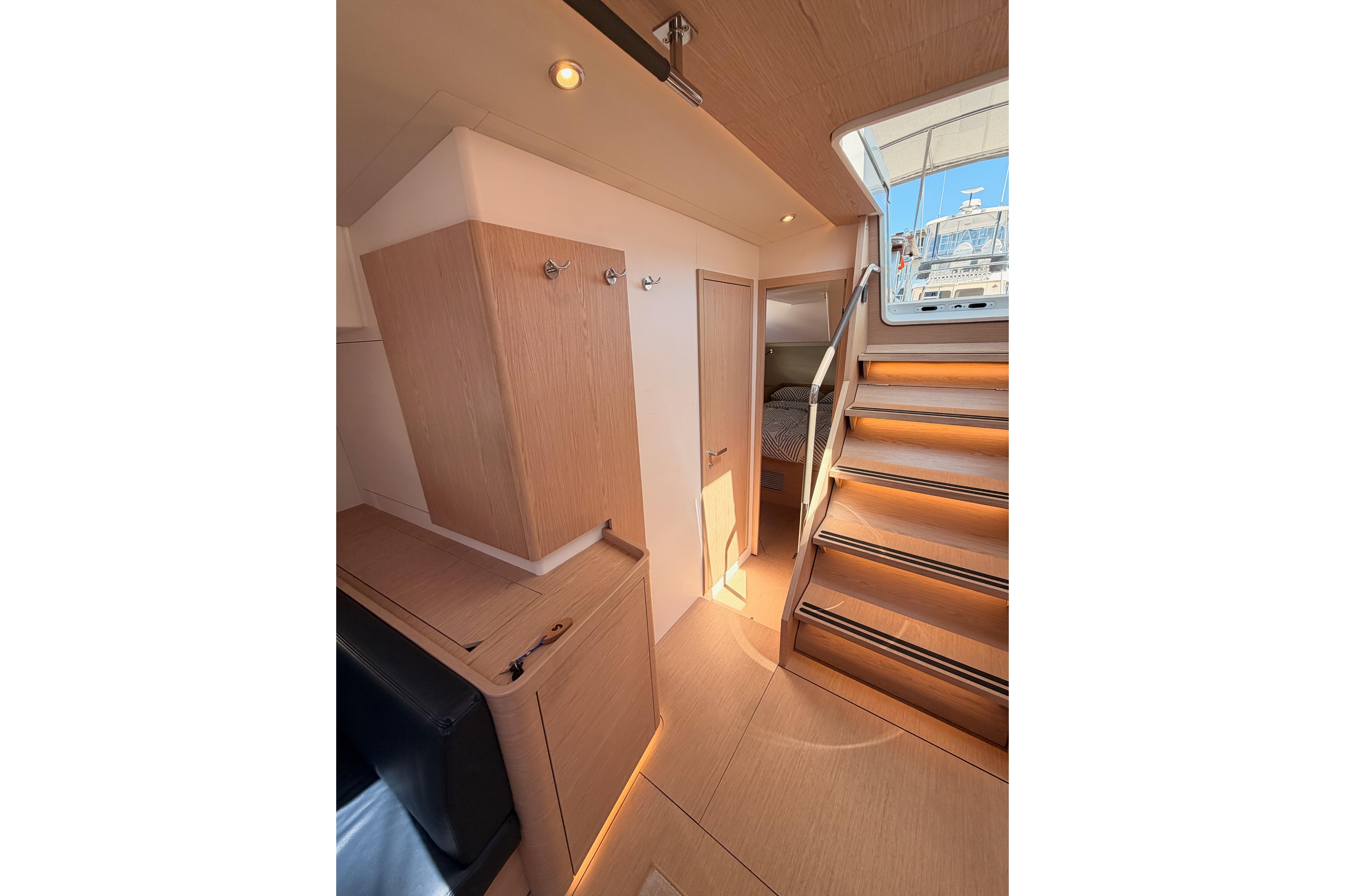 Interior of 2022 Beneteau Oceanis Yacht 54, featuring wooden cabinetry and illuminated stairs.
