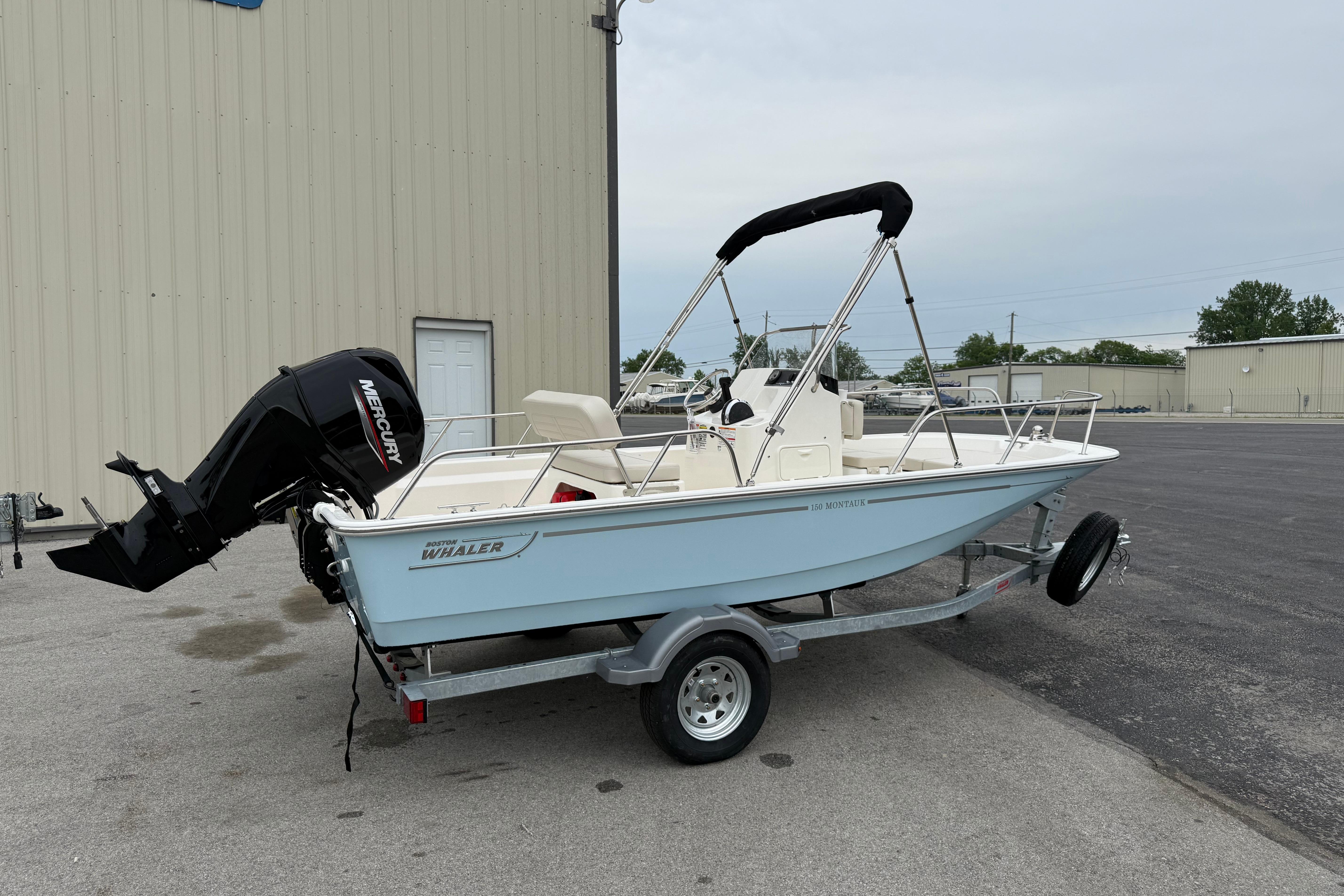2026 Boston Whaler 150 Montauk boat on trailer, parked outdoors near a building.