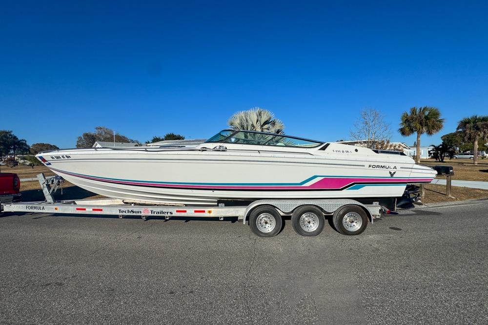 1989 Formula 292 SR-1 boat on trailer, vibrant stripes, clear blue sky background.