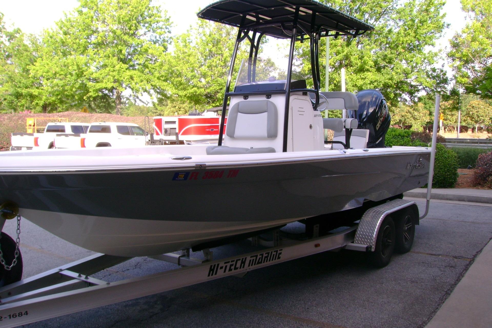 2022 NauticStar 227 XTS boat on trailer, parked outdoors with trees in background.