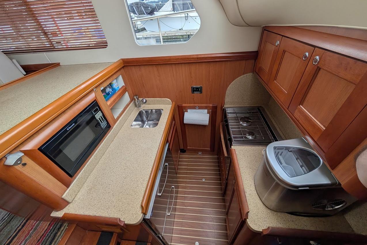 2008 Mainship 38 yacht kitchen with wood cabinets, microwave, sink, and stove.